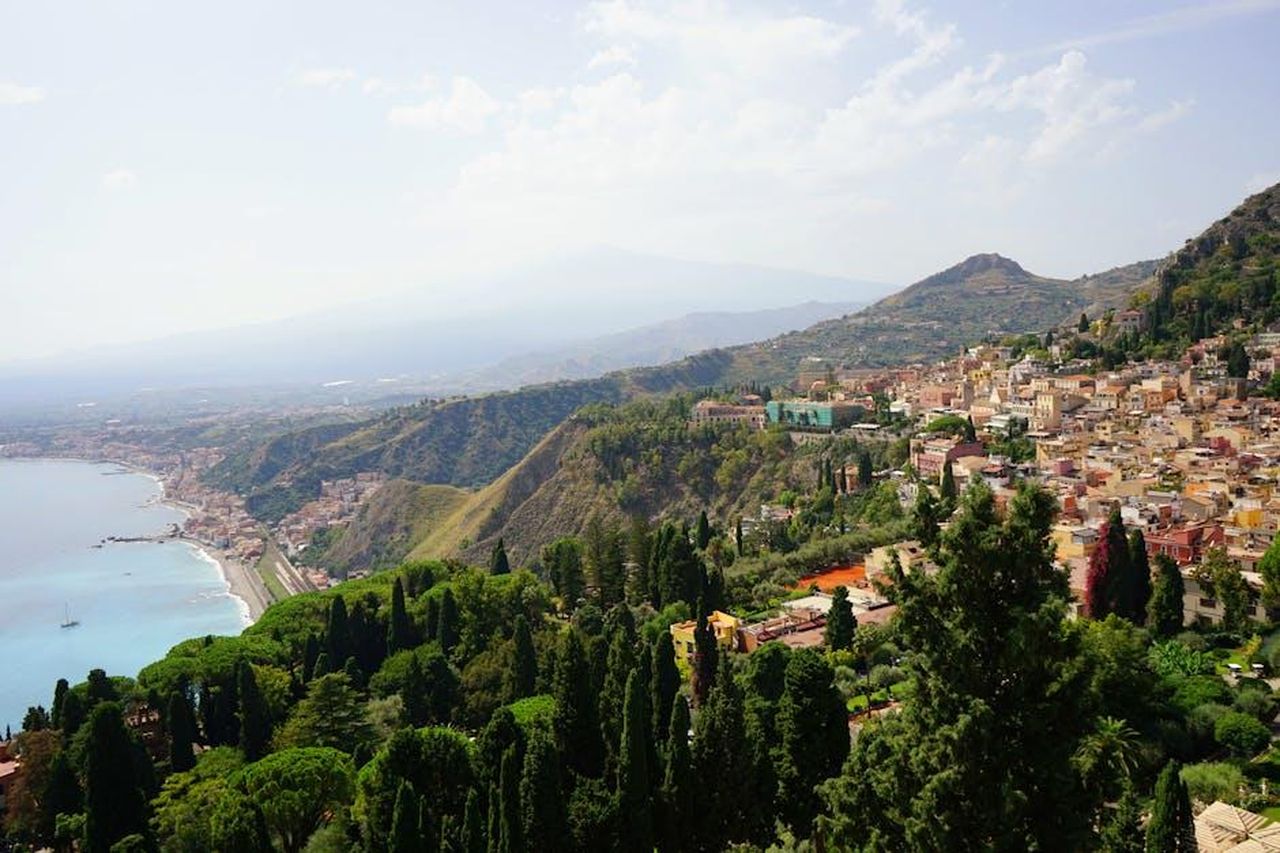 Nessuna_preoccupazione_da_parte_di_Lucio_Presta_per_queste_defezioni_mzWRbCuPxh - Confidenze24 Source: Alexandra Holbea - pexels - A breathtaking view of Taormina, Sicily with lush greenery, coastline, and hills under a summer sky.