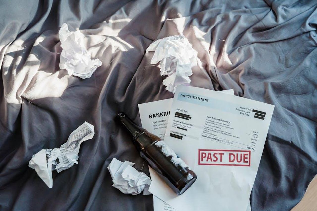 Non_sono_stata_pagata_per_mesi_BAWQBLnSJB - Confidenze24 Source: Nicola Barts - pexels - Scene of financial distress with bankruptcy notice, past due bills, and crumpled papers on a bed.