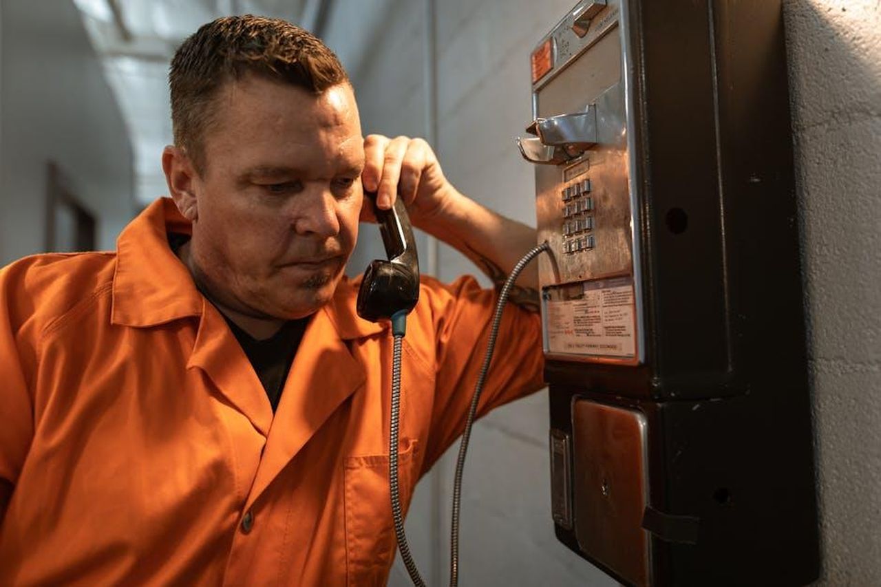 Ozan_viene_scarcerato_i_due_testimoni_lo_scagionano_tSp9RSHBC8 - Confidenze24 Source: RDNE Stock project - pexels - An inmate in an orange jumpsuit makes a phone call inside a prison facility, conveying the prison life atmosphere.