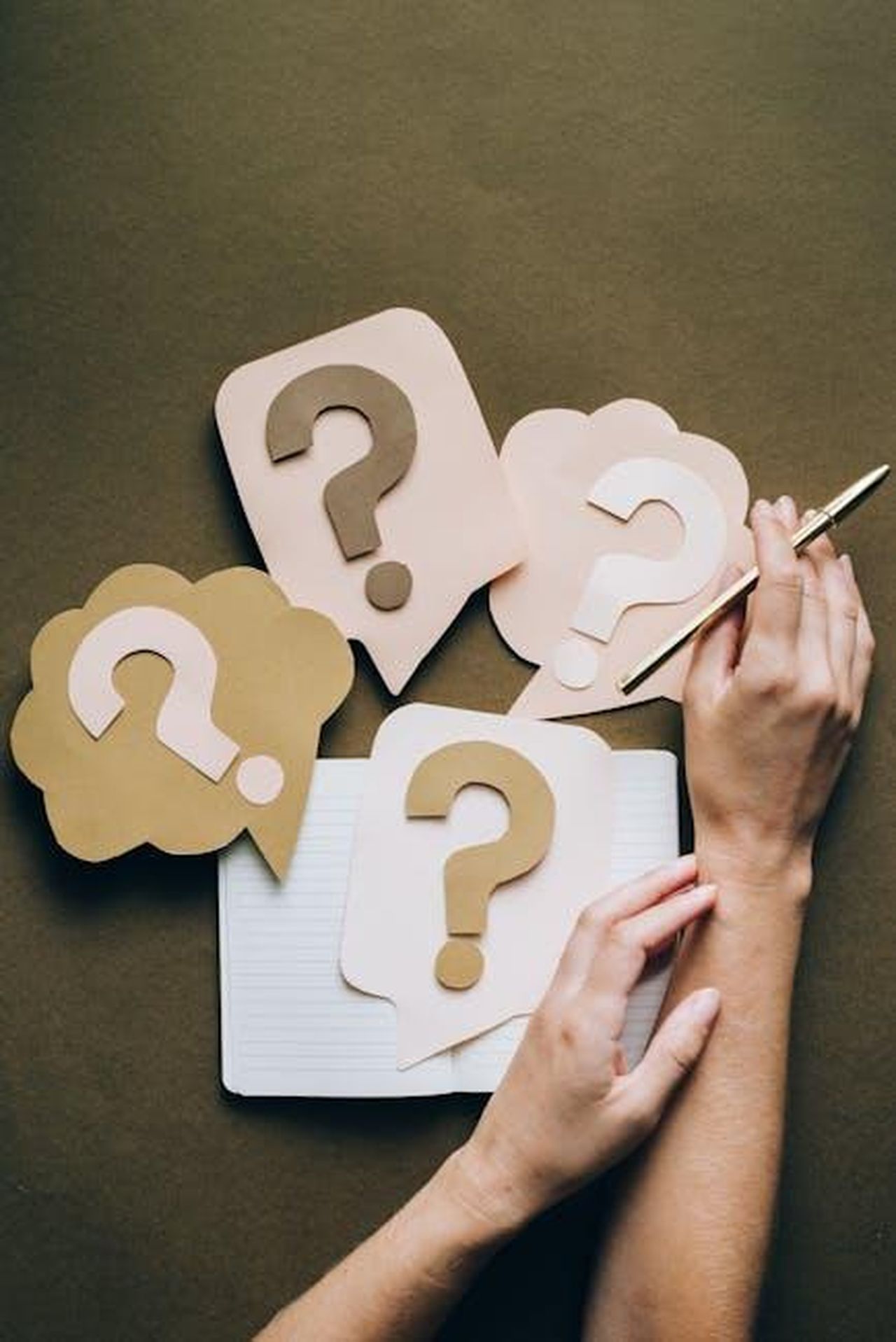 Perch_Olly_ha_deciso_di_non_partecipare_1Fdnu8IgOX - Confidenze24 Source: Leeloo The First - pexels - Hands holding pen next to paper question marks on notebook, symbolizing inquiry and creativity.