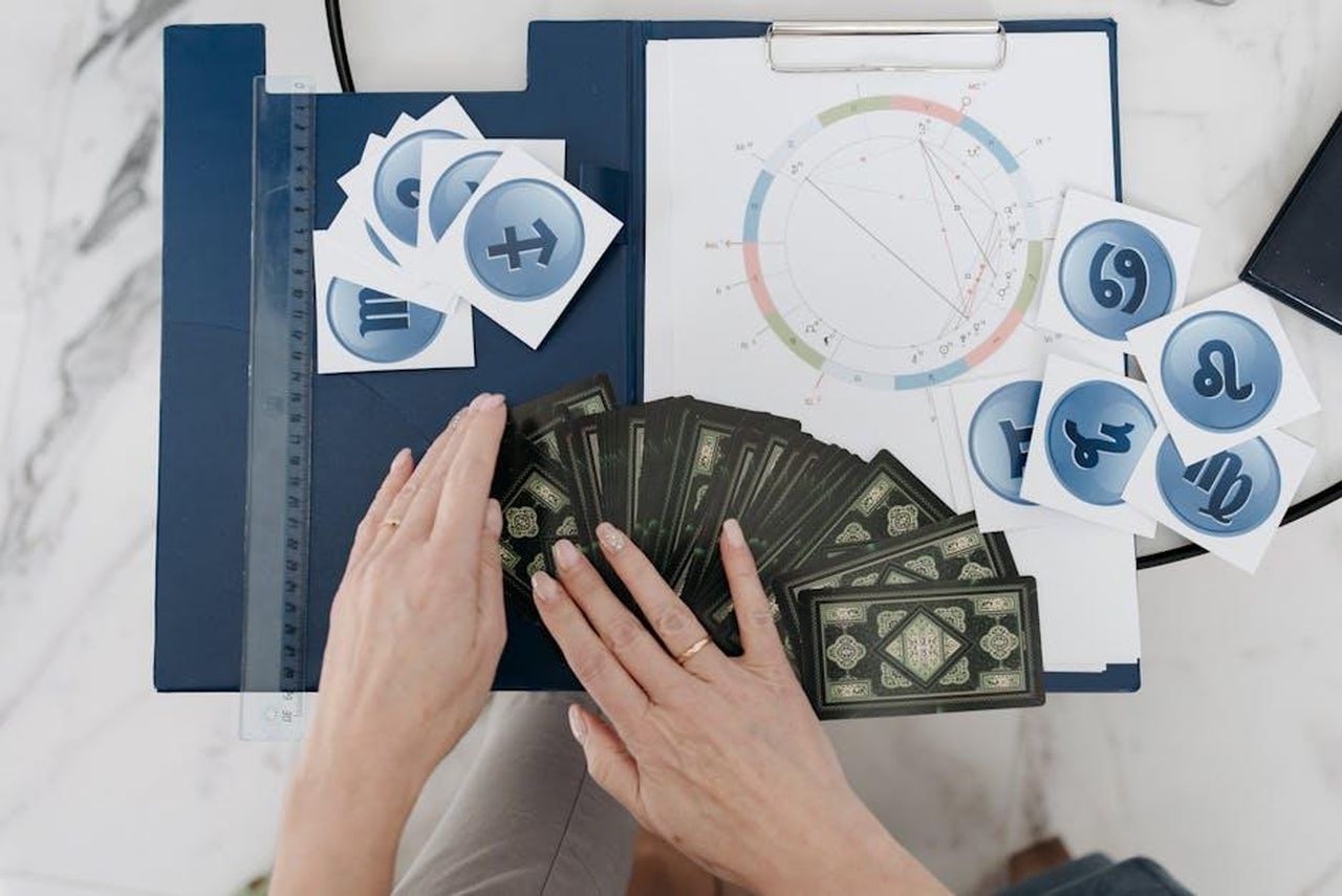 Pesci__5zRfwMjfYP - Confidenze24 Source: Pavel Danilyuk - pexels - Hands arranging tarot cards with astrology symbols and natal chart on a table.