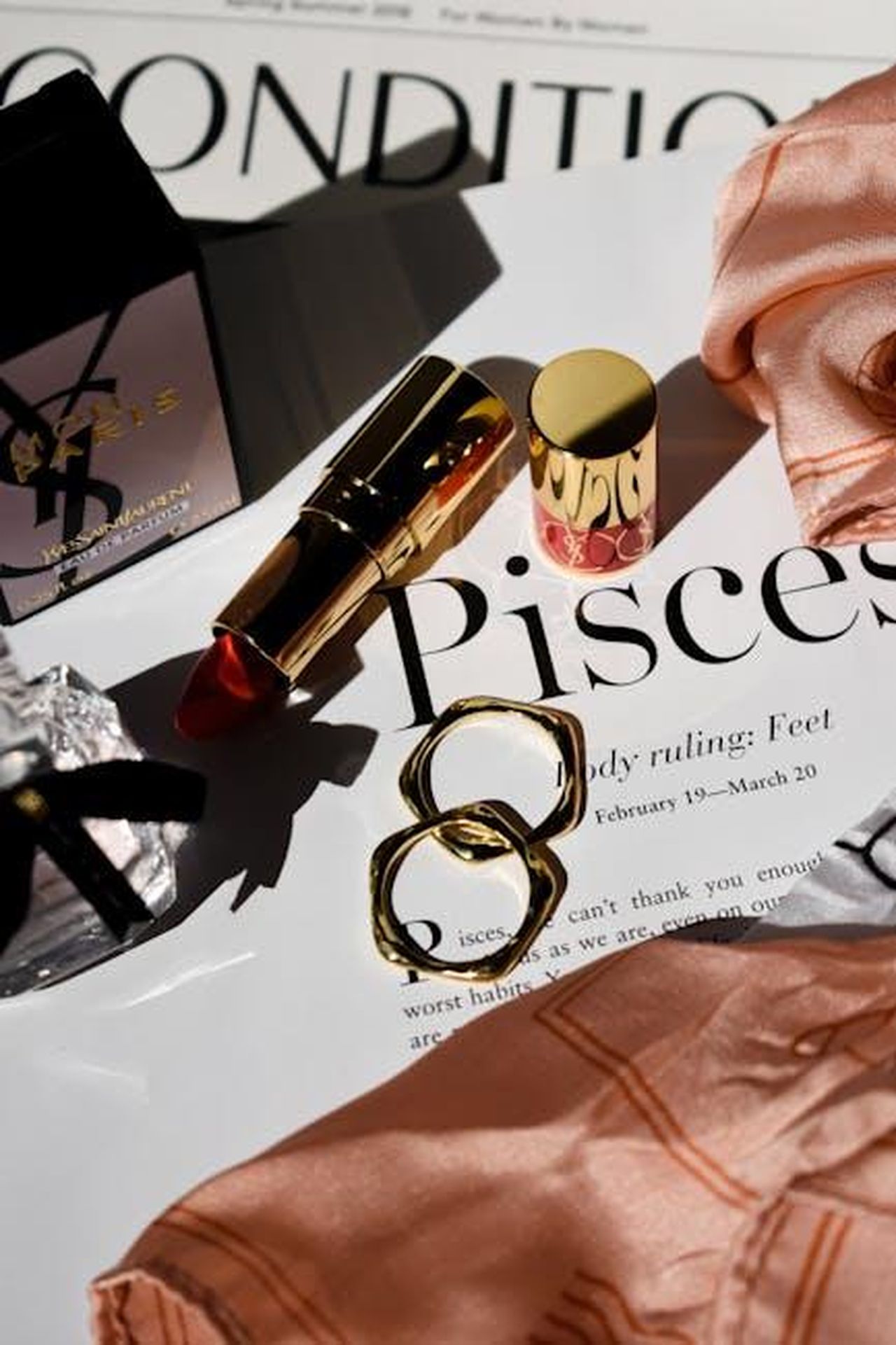 Pesci_complicazioni_sentimentali_e_progetti_lavorativi_ebrrOJenDK - Confidenze24 Source: Harper Sunday - pexels - Stylish flat lay featuring gold lipstick and jewelry on a glamorous magazine page.