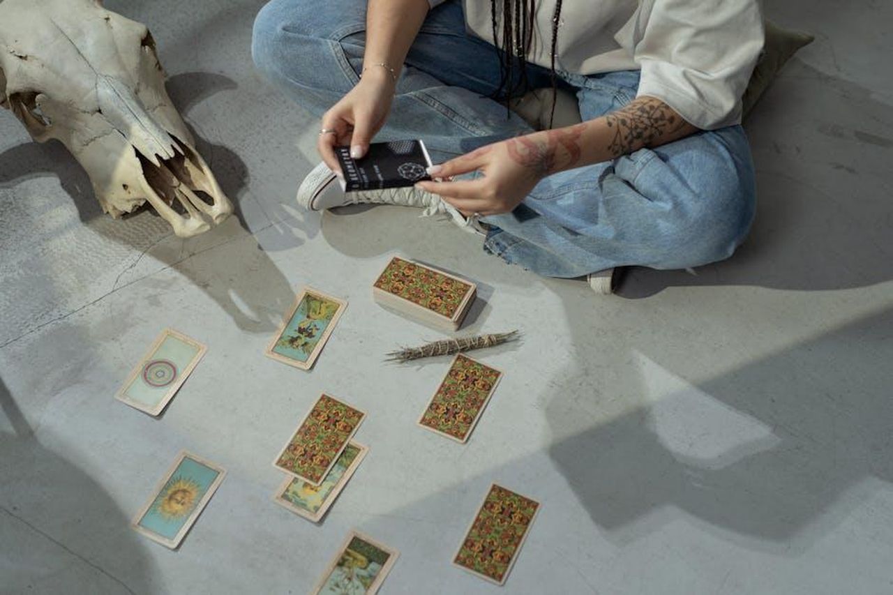 Previsioni_zodiacali_del_18_febbraio_la_coda_della_classifica_g8ysl8BGkh - Confidenze24 Source: cottonbro studio - pexels - A tattooed person sits on the floor performing a tarot reading with cards and a skull.