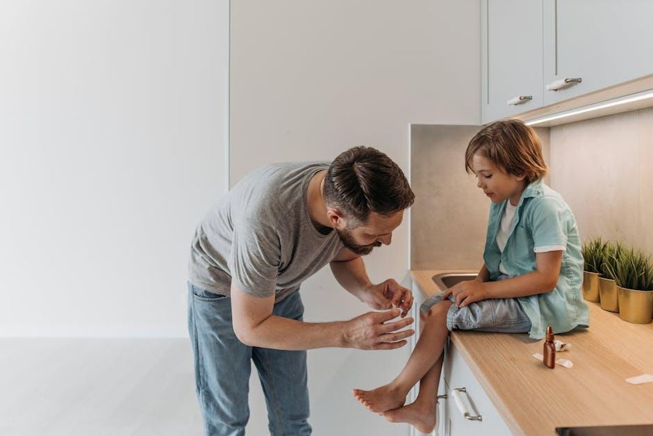Qualcuno_ferisce_gravemente_Ozan_con_dei_colpi_di_pistola_5WqI6n1YAv - Confidenze24 Source: Pavel Danilyuk - pexels - A father is applying a bandage to his son's knee as they sit on a kitchen countertop.