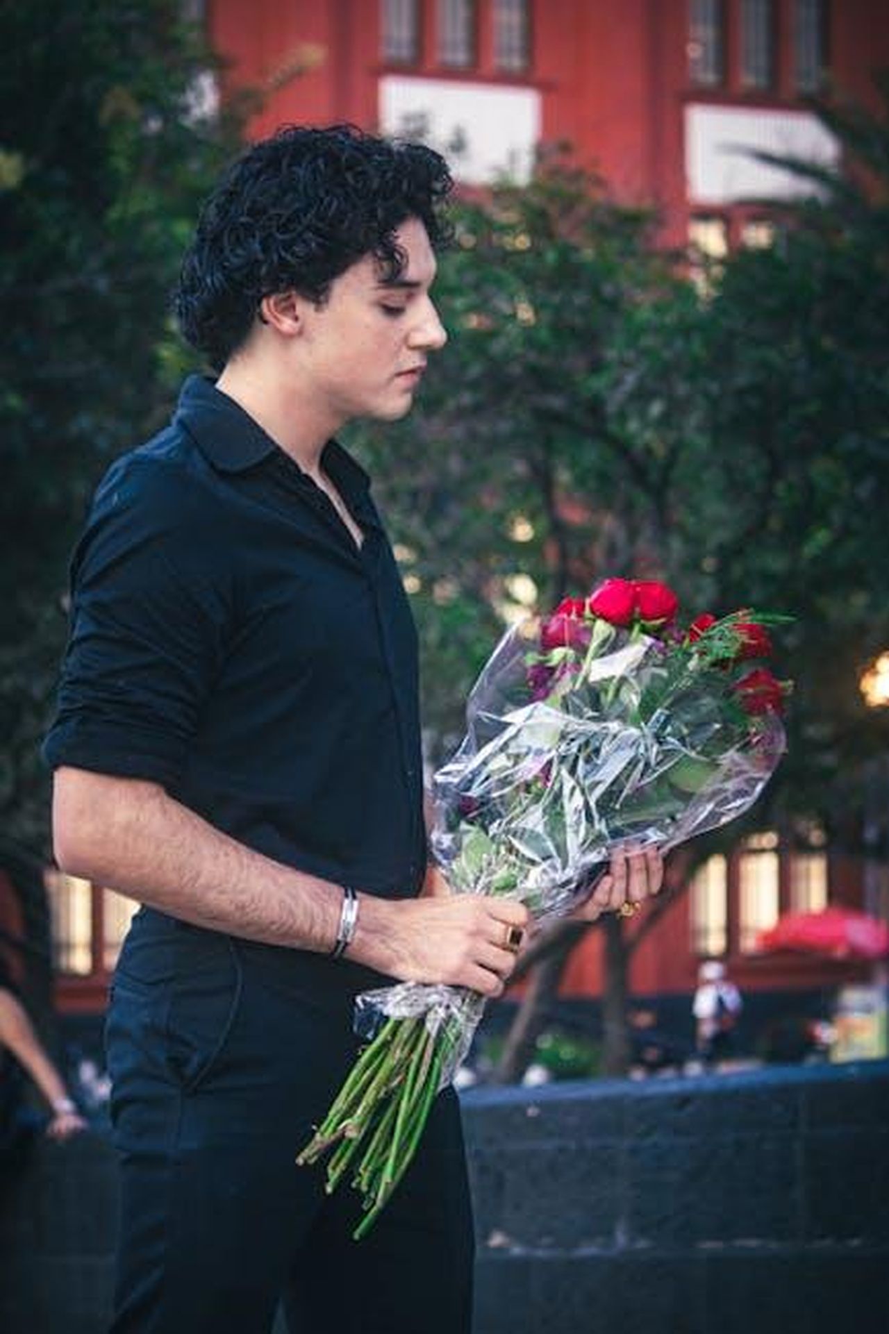 Quando_hanno_iniziato_a_frequentarsi_Erivo_e_Waithe_2ercE2sYb6 - Confidenze24 Source: Moisés Fonseca - pexels - A man in black clothing holds a bouquet of red roses in a city park, conveying romance.
