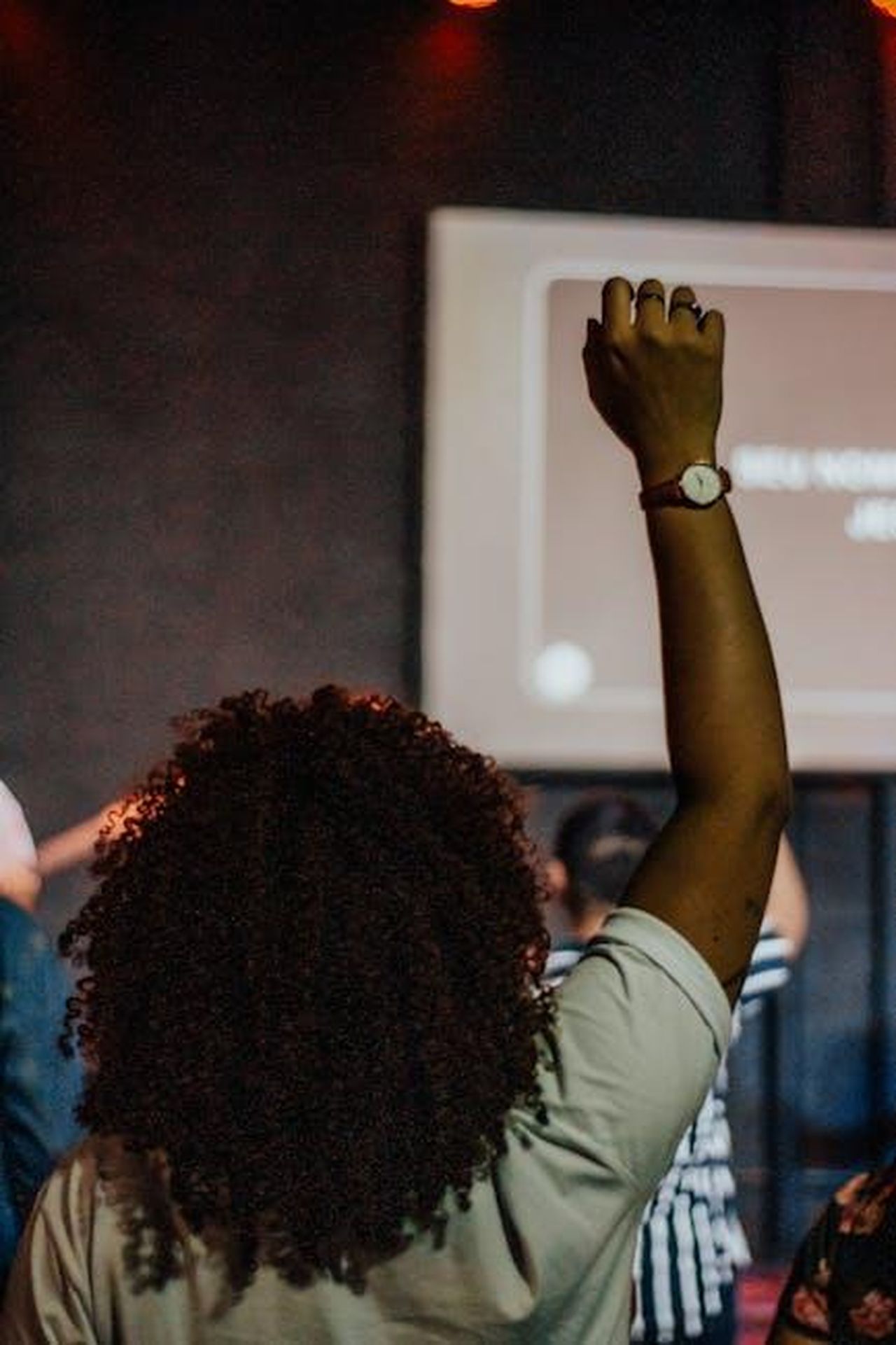 Reazioni_del_pubblico_e_opinioni_sui_comportamenti_di_Tommaso_KJXXHdDM1y - Confidenze24 Source: Igreja Dimensão - pexels - Back view of a person raising hand indoors at a lively event.