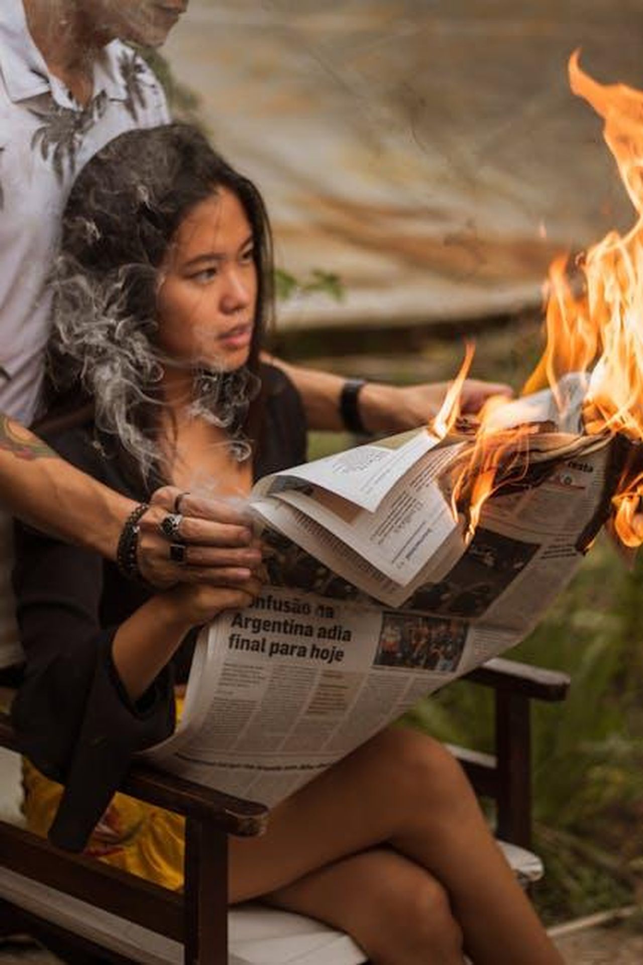 Reazioni_del_pubblico_e_possibili_sviluppi_IVL41d3ZFB - Confidenze24 Source: Matheus Potsclam Barro - pexels - A woman reads a newspaper while it's on fire, creating a dramatic scene with smoke outdoors.