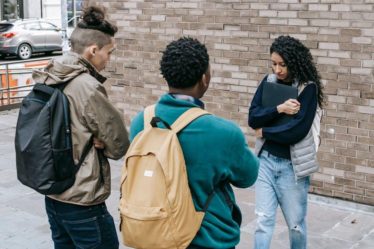 Reazioni_della_comunit_locale_kilJzB1SdG - Confidenze24 Source: Keira Burton - pexels - Young multiracial male friends with backpacks offending female with folder on city street near brick wall in daylight