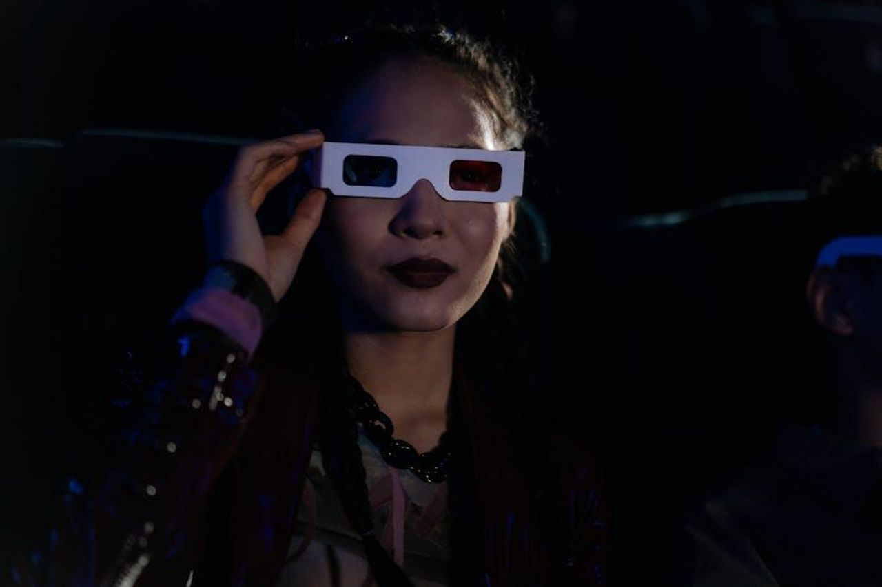 Reazioni_e_aspettative_per_il_film_snWQlJkByw - Confidenze24 Source: cottonbro studio - pexels - A woman in a dark cinema wearing 3D glasses, enjoying an immersive movie experience.