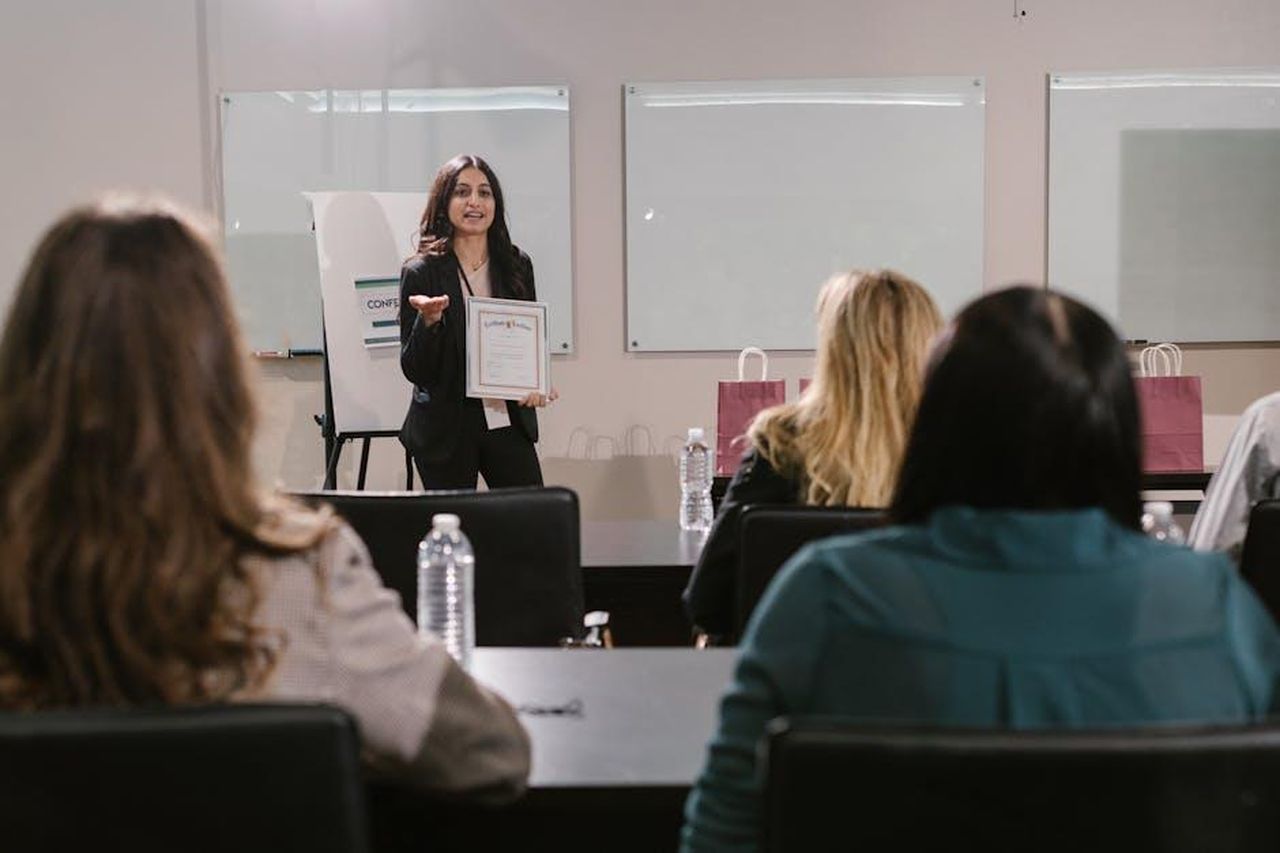 Riconoscimenti_e_premi_85aUfSinf4 - Confidenze24 Source: RDNE Stock project - pexels - A business seminar showcasing a female presenter awarding certificates to attendees.