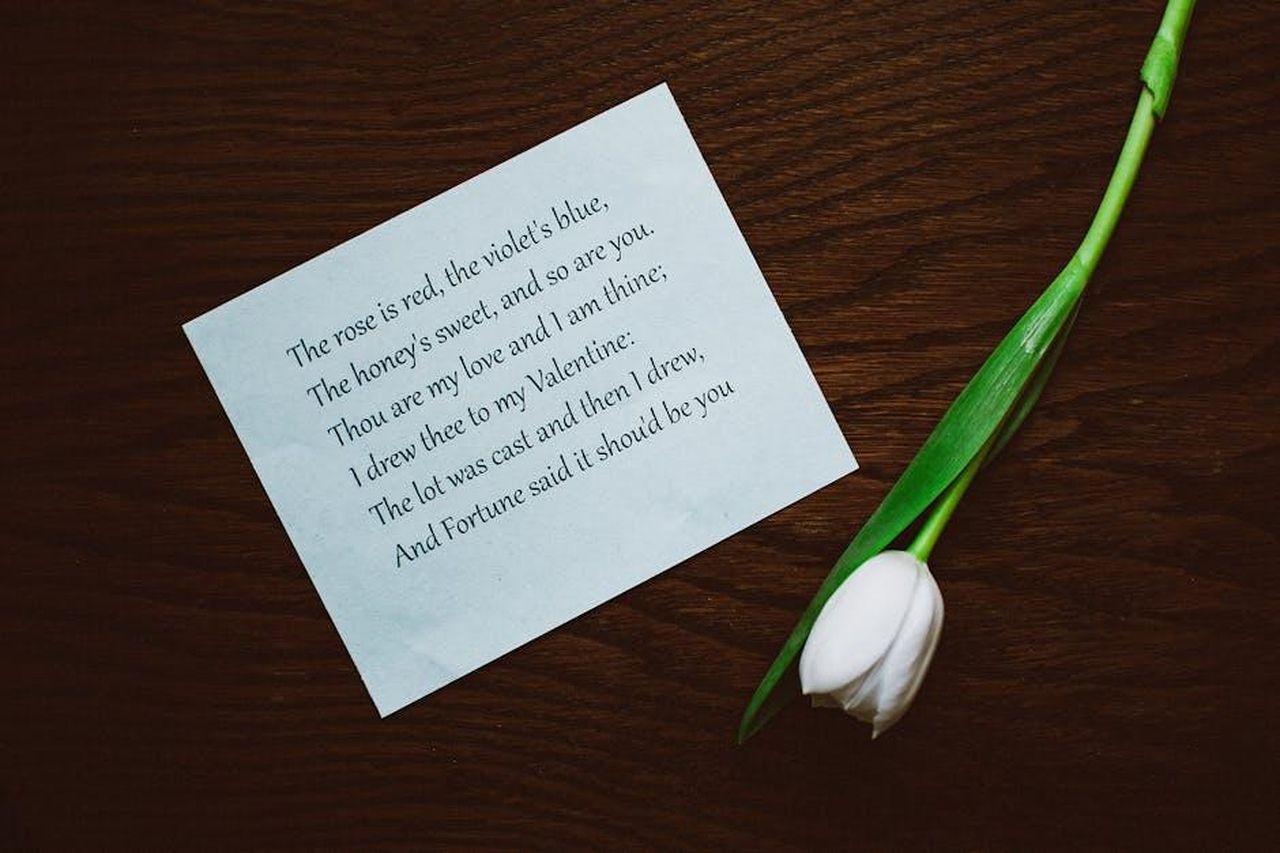 Ricorrenze_ed_eventi_durante_il_Salone_Tlyj7j5EN2 - Confidenze24 Source: Lisa Fotios - pexels - A Valentine's Day poem beside a white tulip on a dark wooden table, evoking romance.