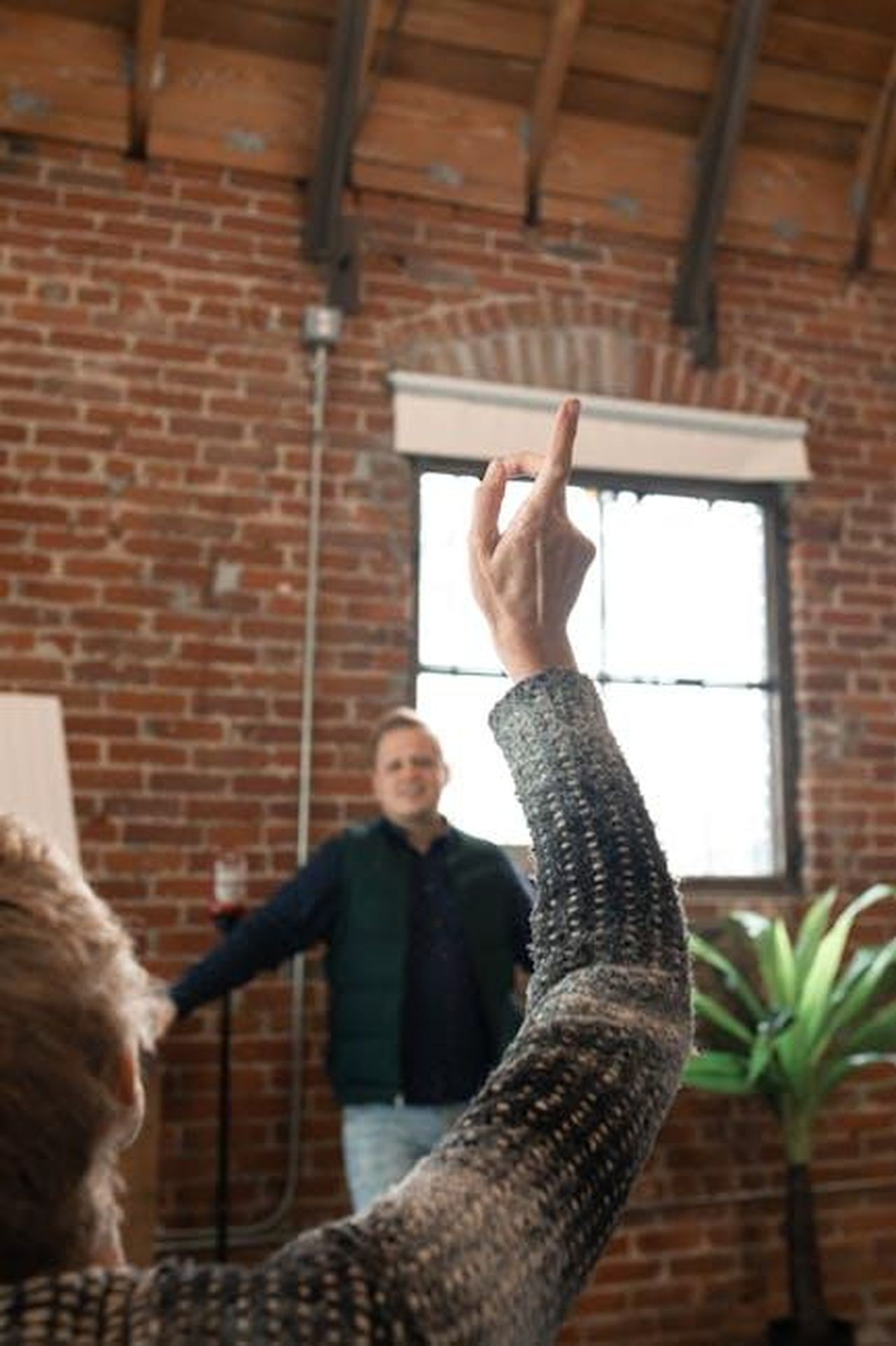 Risposta_del_pubblico_e_reazioni_degli_artisti_89XsosIX8C - Confidenze24 Source: RDNE Stock project - pexels - A person raising their hand during an indoor presentation with a brick wall background.