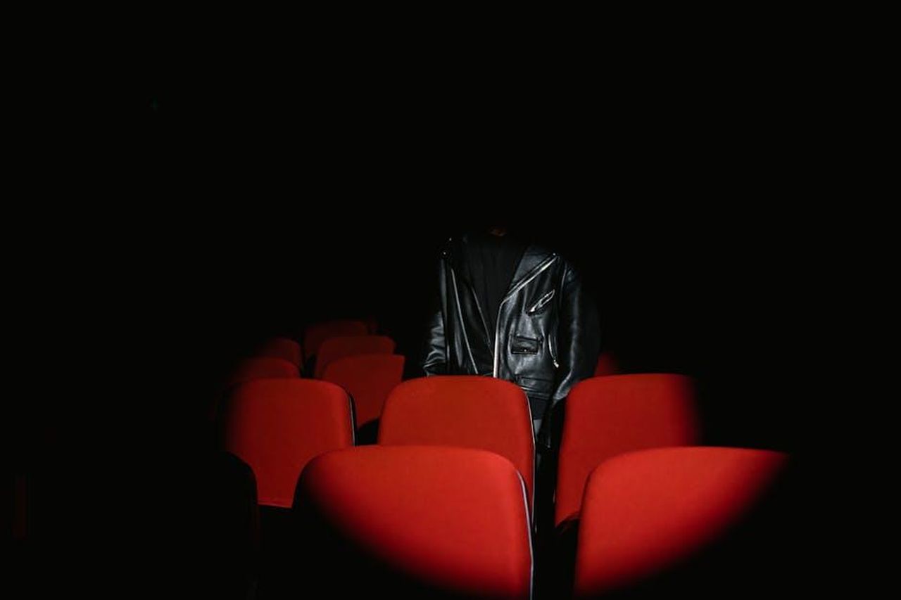 Roberto_scopre_la_storia_di_Marta_anticipazioni_Il_Paradiso_delle_signore_25_febbraio_BdY5bSchCe - Confidenze24 Source: Tima Miroshnichenko - pexels - A person in a leather jacket stands among red theater seats in a dark room.