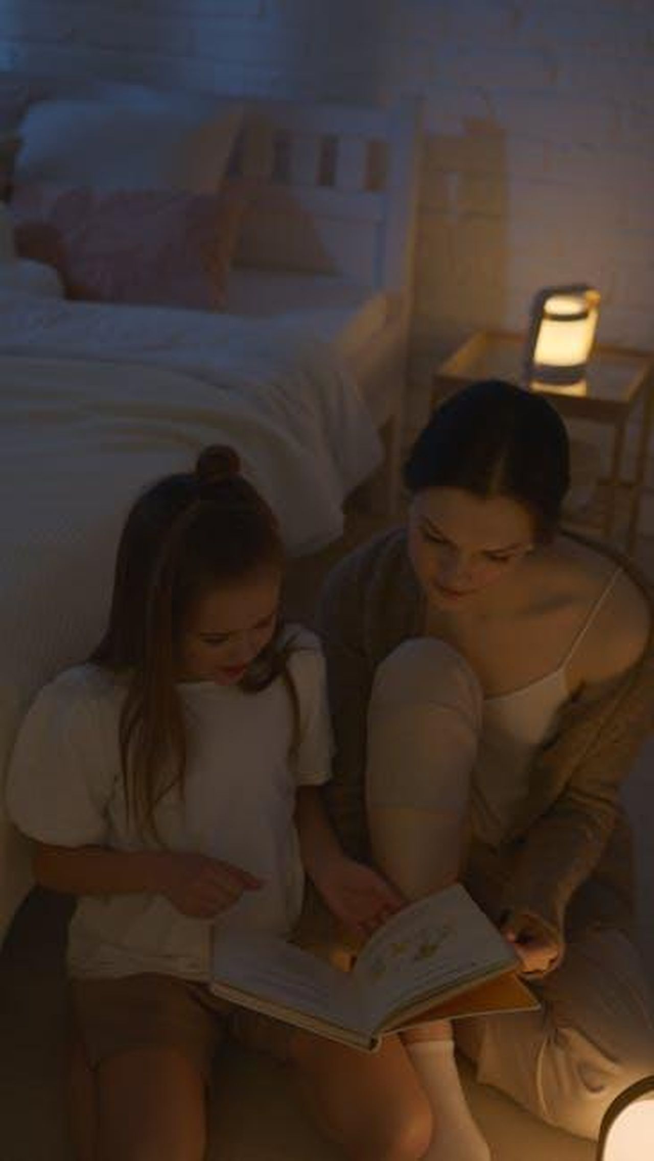 Rosa_e_Pino_sempre_pi_complici_nls4FLvm9q - Confidenze24 Source: Artem Podrez - pexels - A mother and daughter share a warm moment reading a storybook by lamplight in a cozy bedroom setting.