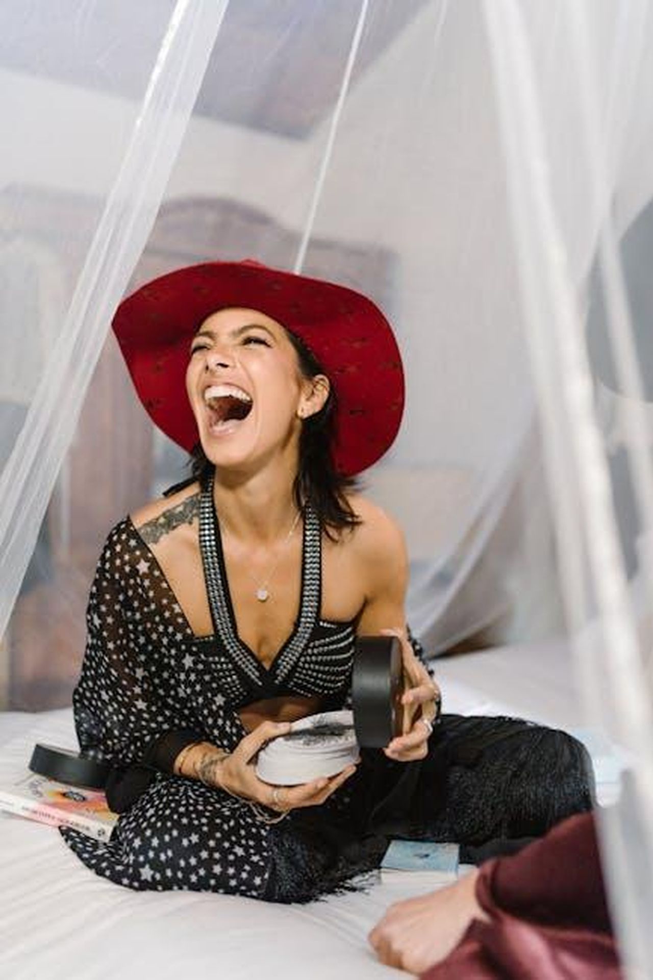 Sagittario_22_novembre__21_dicembre_bdU10DEMhZ - Confidenze24 Source: RDNE Stock project - pexels - A woman laughing joyfully while holding tarot cards and crystals, sitting indoors with a vibrant red hat.
