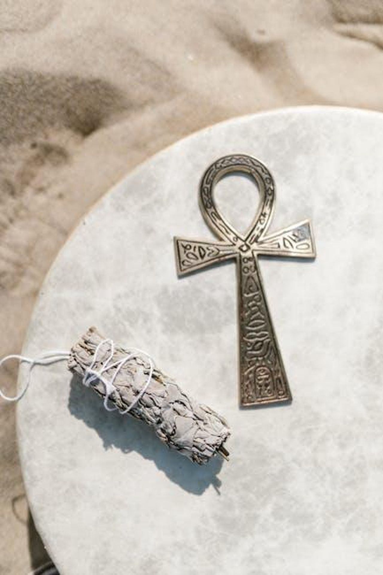 Sagittario_piani_professionali_a_rischio_74kr2a8Ajn - Confidenze24 Source: RDNE Stock project - pexels - A detailed ankh symbol with sage bundle on a textured sandstone surface, evoking spiritual themes.