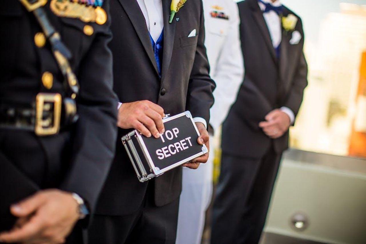 Santos_scopre_il_segreto_di_Lope_wNIUOCQlOp - Confidenze24 Source: Caleb Oquendo - pexels - A group of men in formal military and business attire holding a 'Top Secret' briefcase indoors.