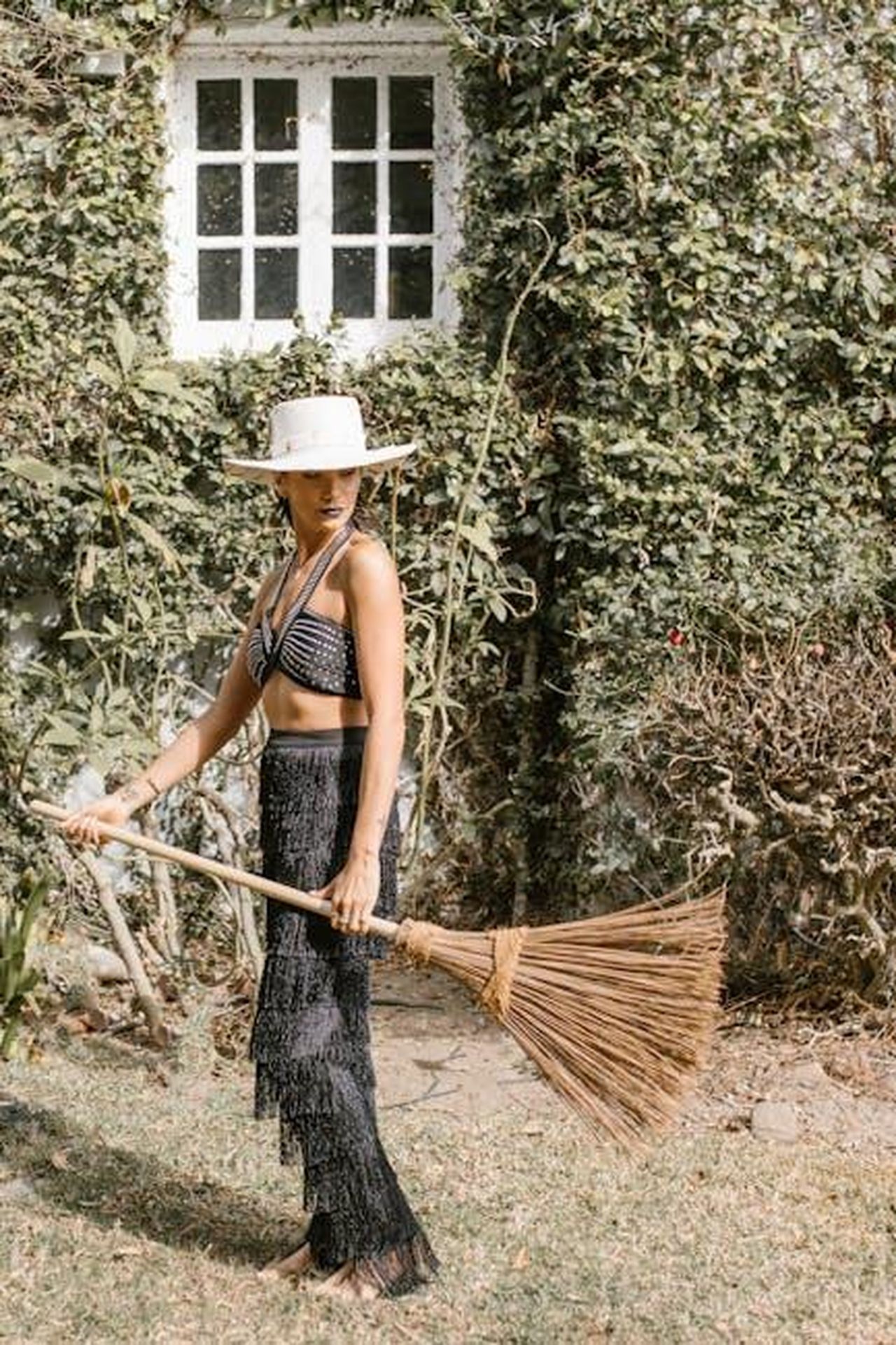 Scorpione_amore_appagante_3JWviXexJK - Confidenze24 Source: RDNE Stock project - pexels - A woman wearing a hat and black outfit sweeps outdoors with a rustic broom beside ivy-covered wall.