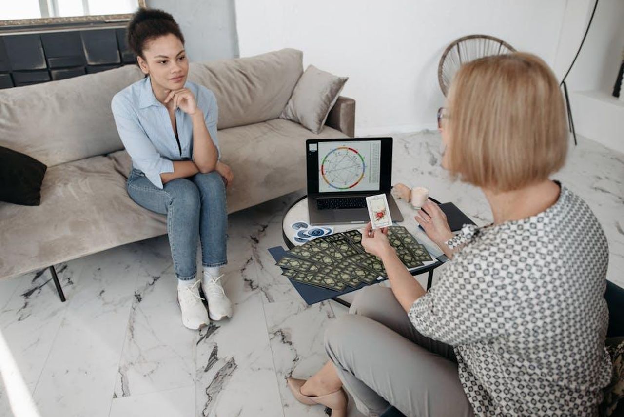 Segni_al_centro_della_graduatoria_qFSCFSpEEd - Confidenze24 Source: Pavel Danilyuk - pexels - Women discuss astrology with a natal chart and tarot cards on a couch.