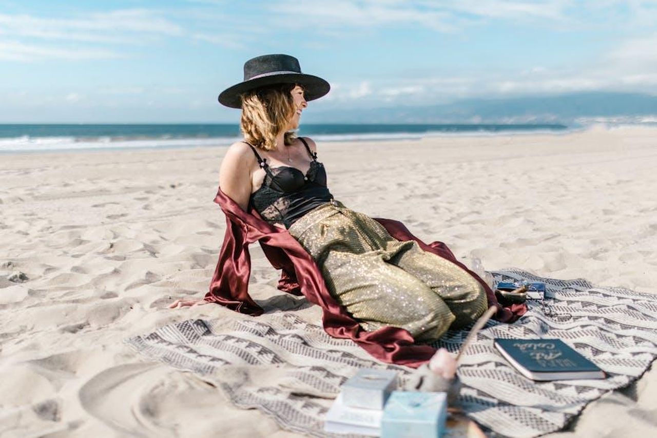 Segni_di_Aria_Gemelli_Bilancia_Acquario_3yNU8vSYXm - Confidenze24 Source: RDNE Stock project - pexels - A woman in a hat sits on a beach surrounded by tarot cards, enjoying the sunny day.
