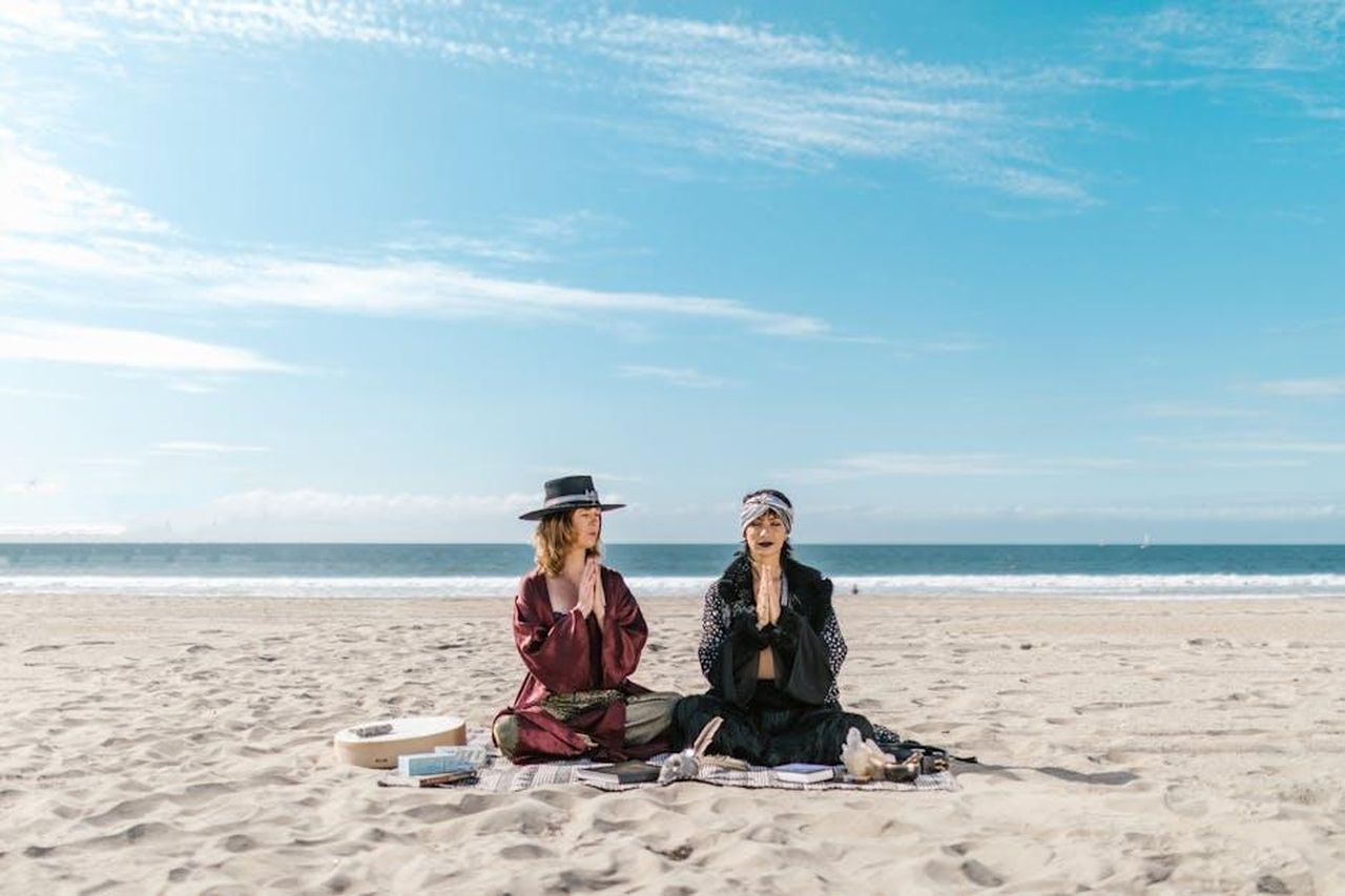 Segni_di_Fuoco_Ariete_Leone_Sagittario_NbLkJsemhB - Confidenze24 Source: RDNE Stock project - pexels - Two women meditating on a serene beach with spiritual items.