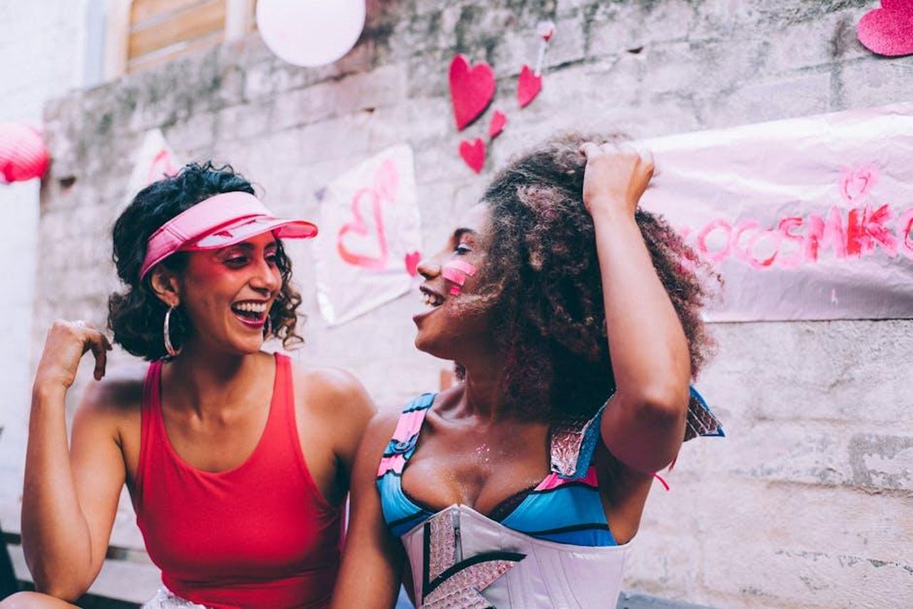Sezai_soffre_perch_pensa_che_Guzide_non_ricambi_il_suo_amore_EmwFH2nnwD - Confidenze24 Source: Laura Stanley - pexels - Two women laughing together at a colorful outdoor celebration with heart decorations.