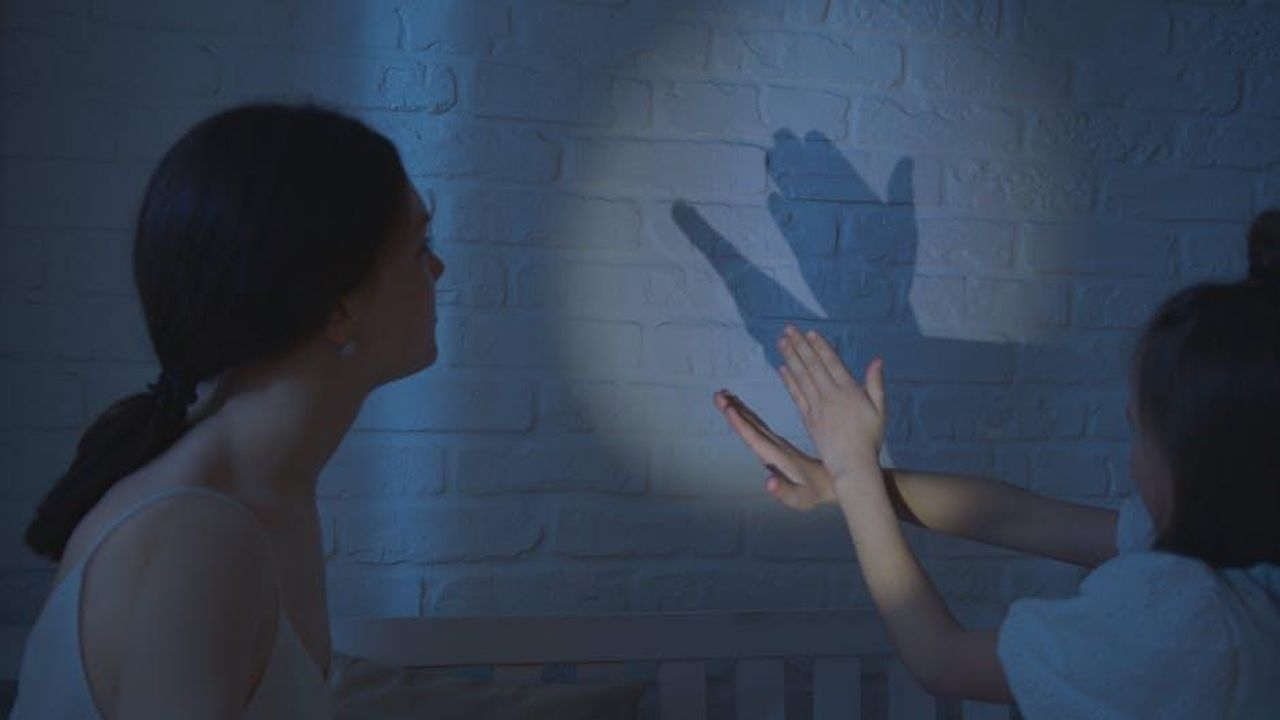 Shaila_a_rischio_eliminazione_rlFJCymrVZ - Confidenze24 Source: Artem Podrez - pexels - A mother and child creating shadow puppets on a bedroom wall under soft lighting.