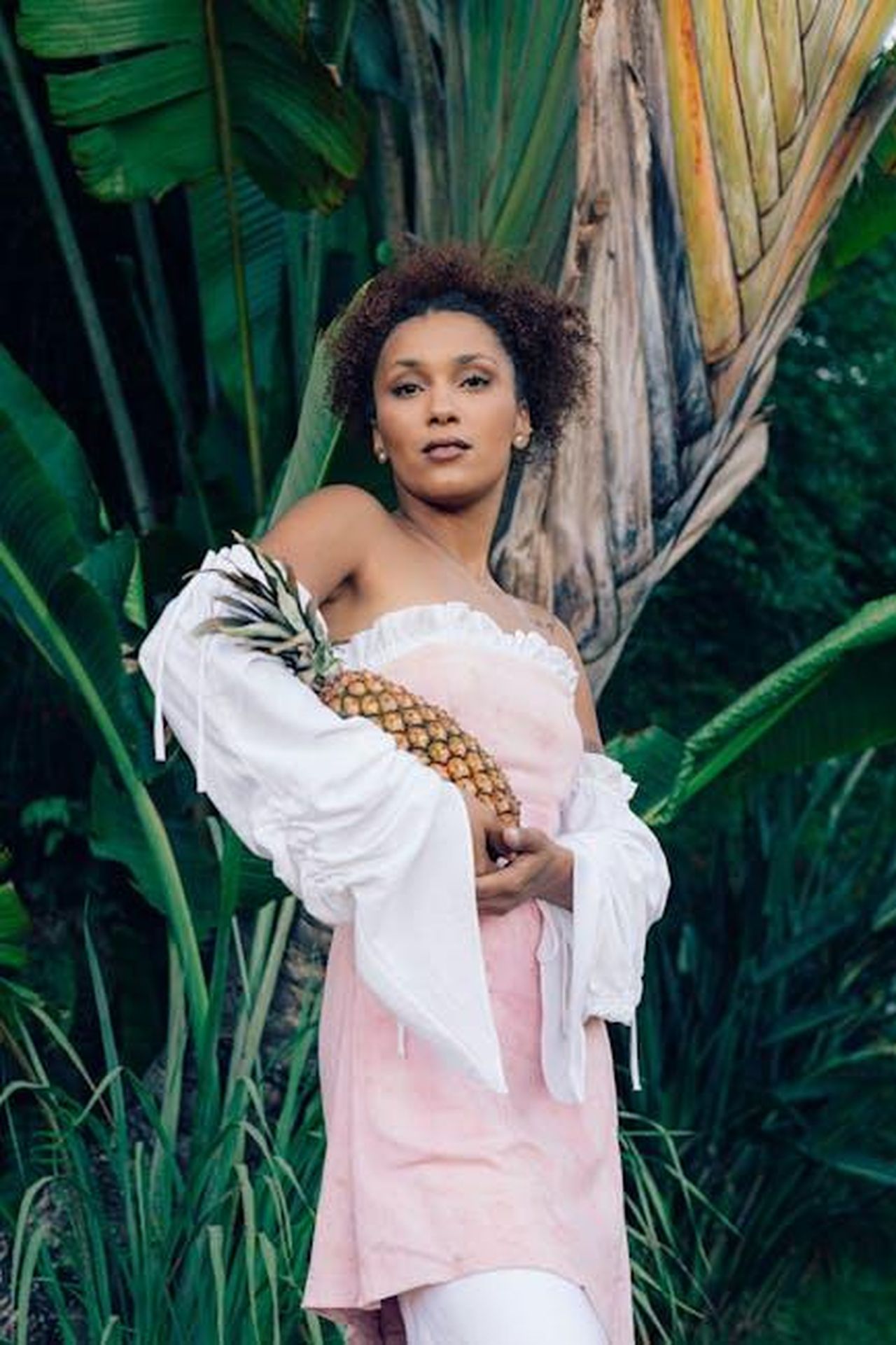 Storia_e_atmosfera_di_Mustique_uBx5NB2DE7 - Confidenze24 Source: Bruna Corrêa - pexels - Elegant woman in tropical setting holding a pineapple, vibrant and natural.