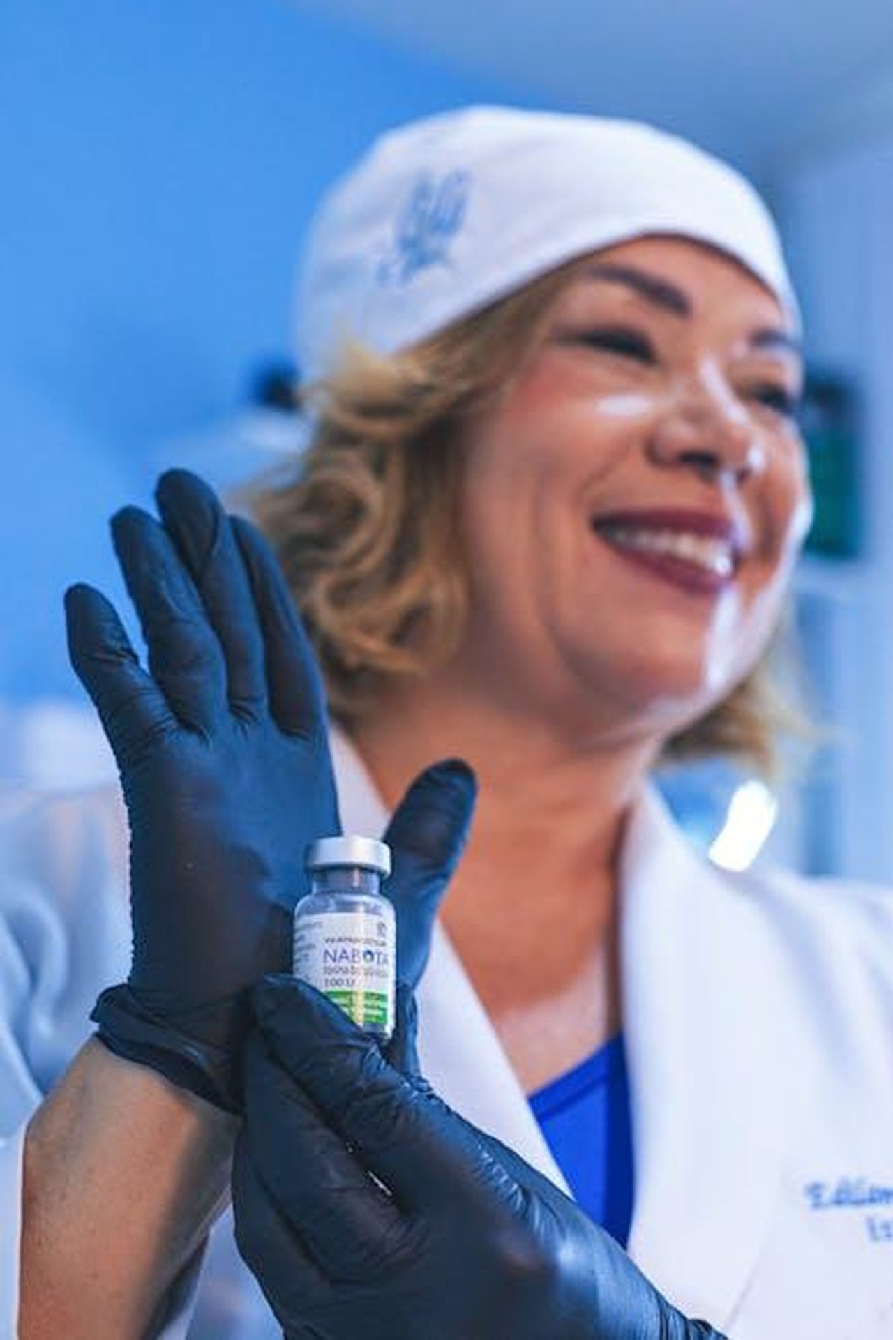 Tassi_di_vaccinazione_in_calo_QGxW3JCErM - Confidenze24 Source: Eric Moura - pexels - Smiling healthcare worker holding a vaccine vial labeled NAOBOT in a clinic setting.