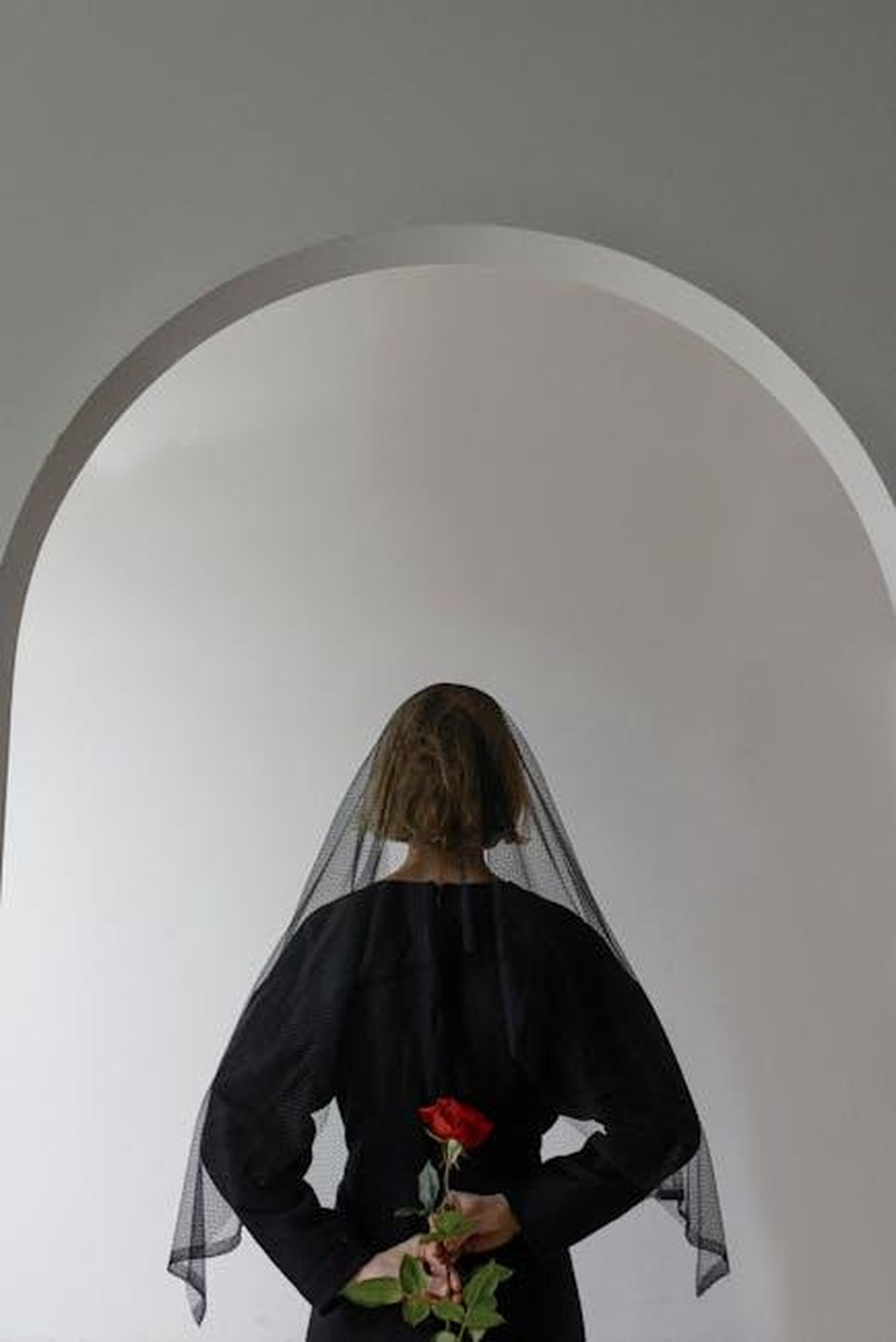 Tieni_cari_coloro_che_ami_MM3UiyglLq - Confidenze24 Source: Ksenia Chernaya - pexels - A woman in a black dress holds a red rose, symbolizing loss and remembrance.