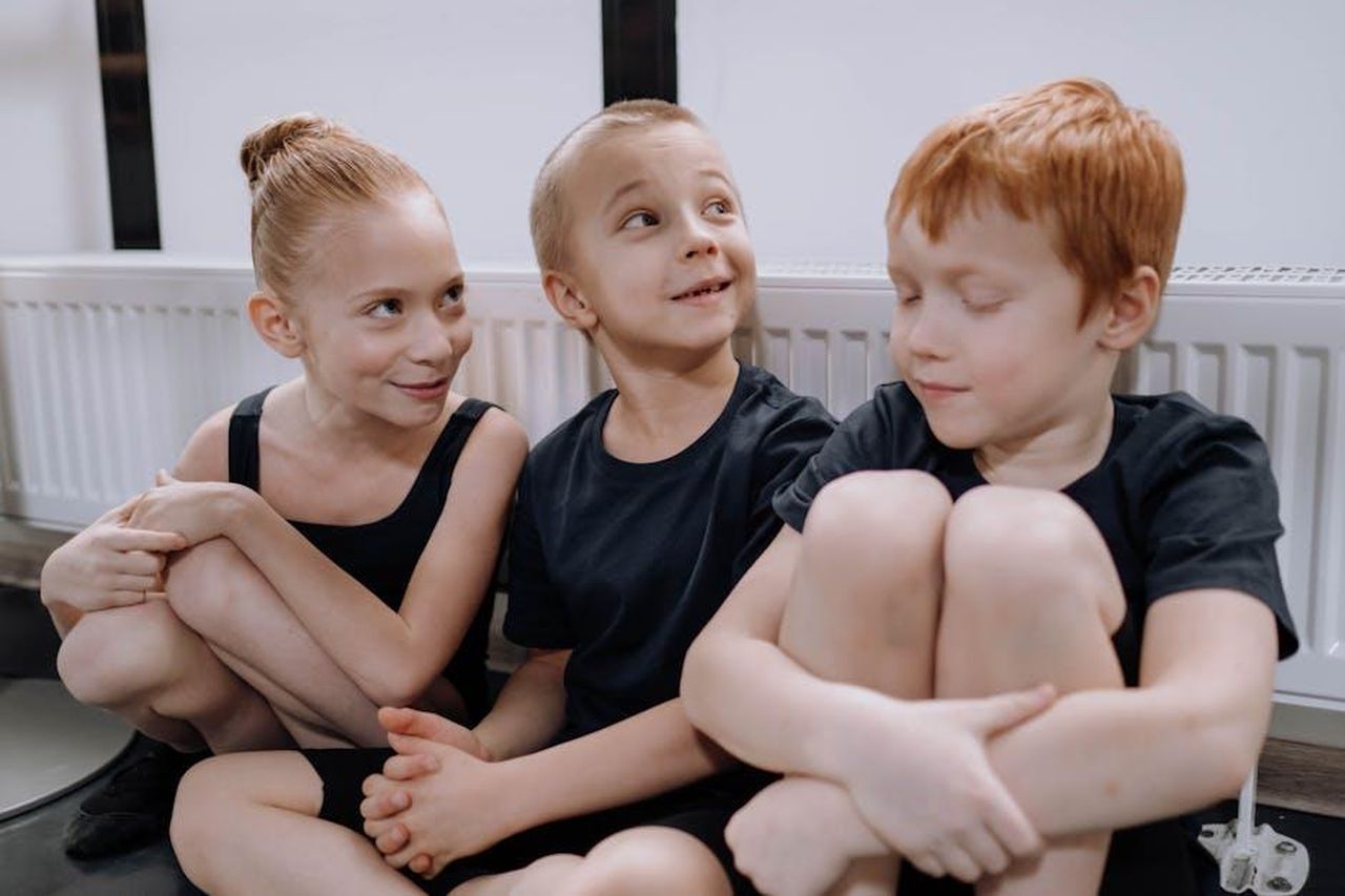 Tildy_inizia_la_ginnastica_PrC50XZkg4 - Confidenze24 Source: cottonbro studio - pexels - Three children sit joyfully on a floor indoors, dressed in black dance clothing.
