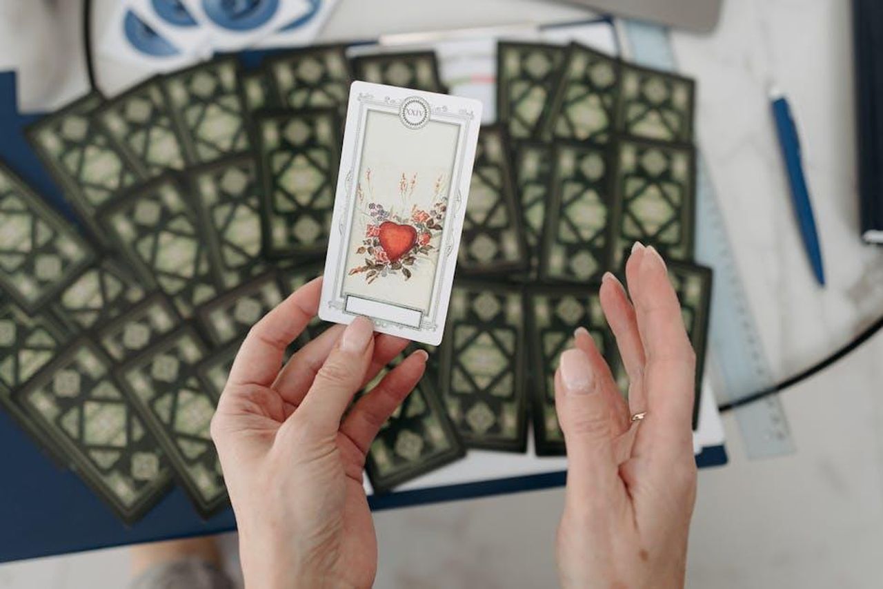 Toro__La_solidit_che_costruisce_il_futuro_fsOQQ4mfby - Confidenze24 Source: Pavel Danilyuk - pexels - Hands holding a tarot card with heart design, surrounded by scattered cards emphasizing mystery.