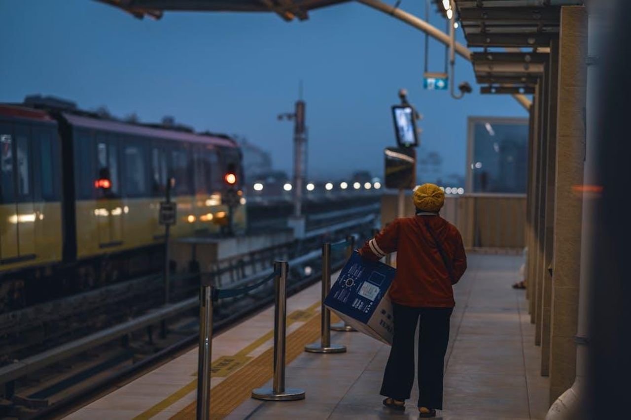 Tradimento_in_onda_alle_ore_1515_sabato_22_febbraio_dpJma0d56Z - Confidenze24 Source: Toàn Văn - pexels - A person at an outdoor train station during twilight, holding a large package.