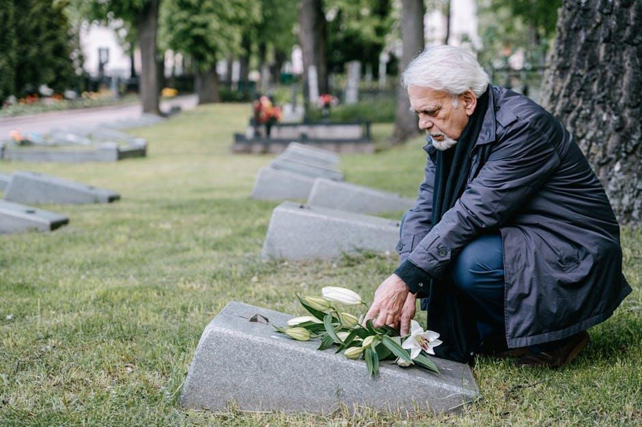 Tributi_in_arrivo_xeSnw9iAge - Confidenze24 Source: Ivan Samkov - pexels - Senior man with white hair honorably placing lilies on a grave in a peaceful cemetery setting.