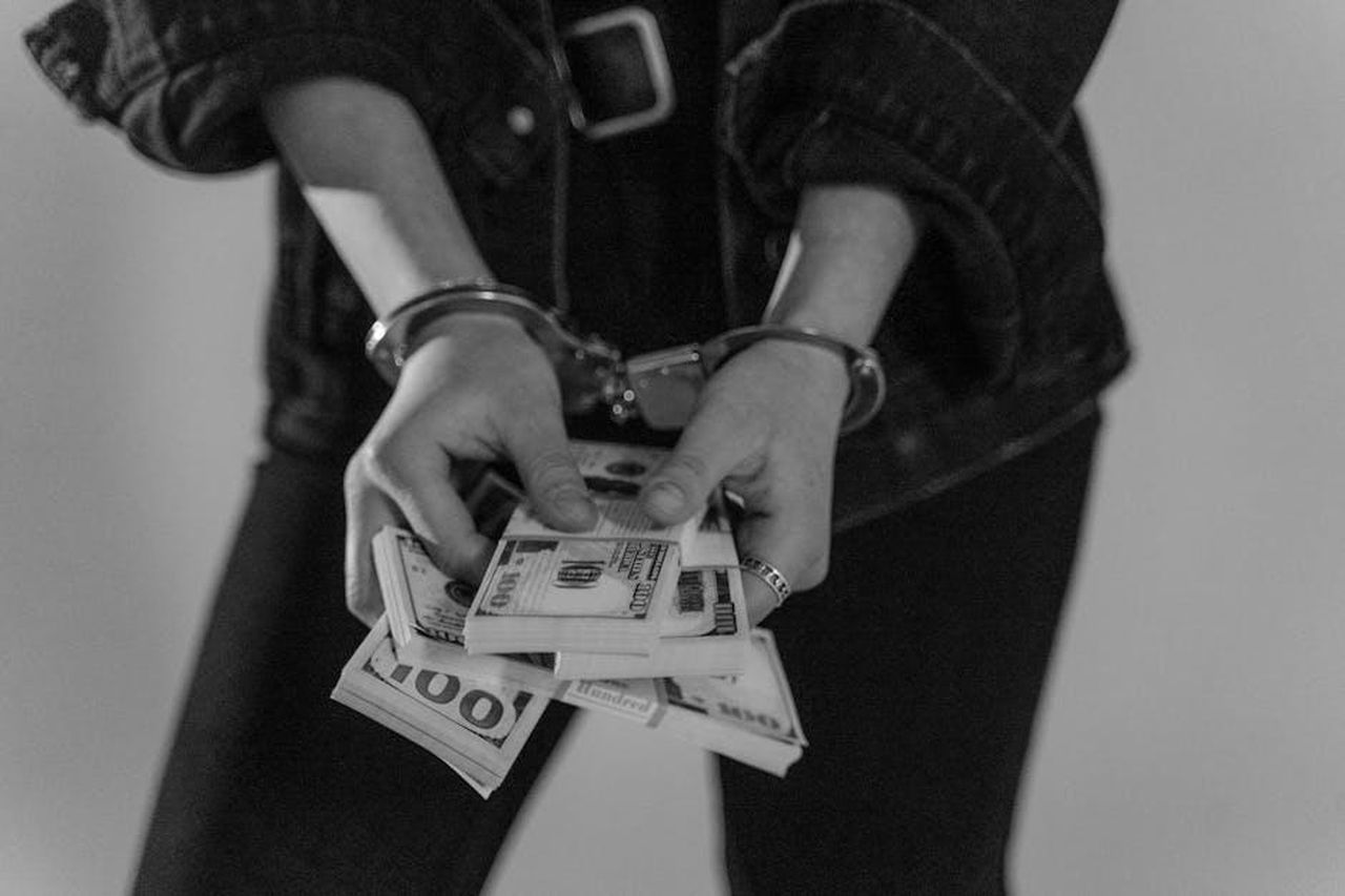 Umit_finisce_in_arresto_con_laccusa_di_sequestro_uOfzmfuZaI - Confidenze24 Source: Tima Miroshnichenko - pexels - Black and white image of a handcuffed person holding bundles of US dollars.