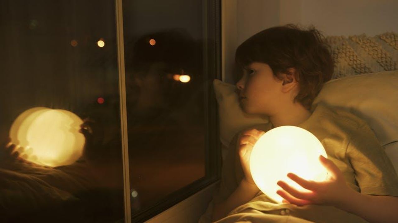 Un_momento_di_tregua_nella_Casa_jKW58SJVdH - Confidenze24 Source: Artem Podrez - pexels - A young boy holding a glowing orb, looking out a window at night.