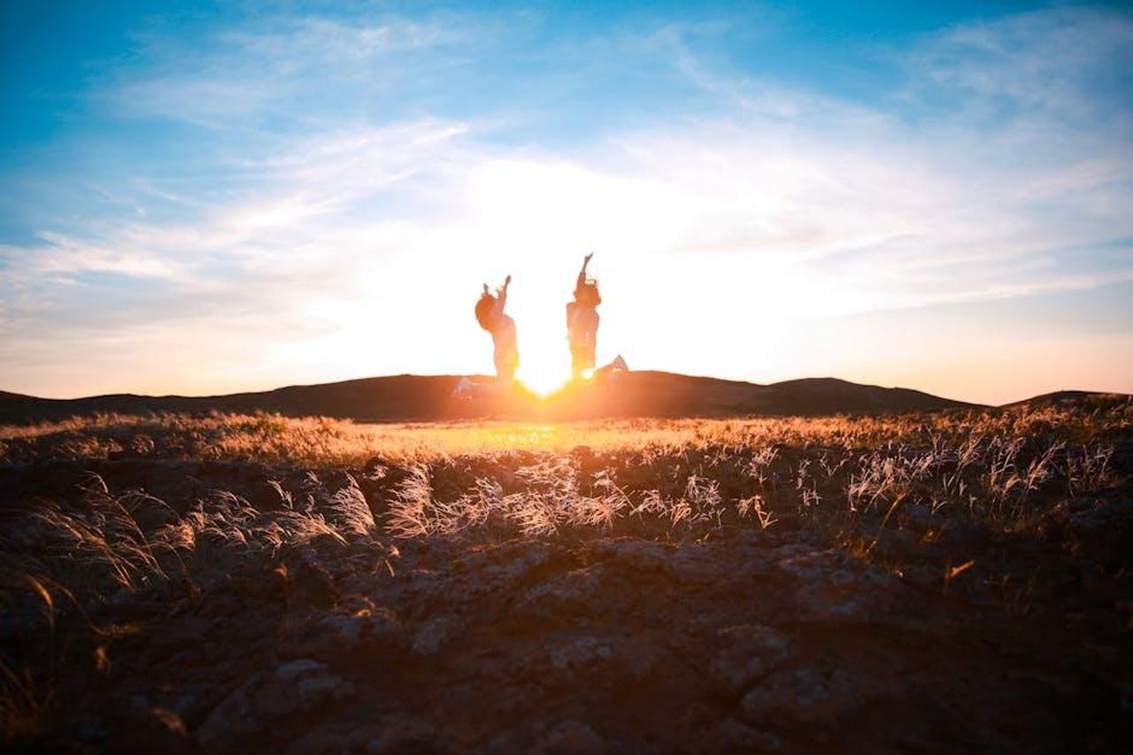 Unamicizia_che_resiste_al_tempo_Q61Z7w58sc - Confidenze24 Source: Hakan Hu - pexels - Two friends silhouette jumping in a scenic field at sunset, celebrating nature and friendship.