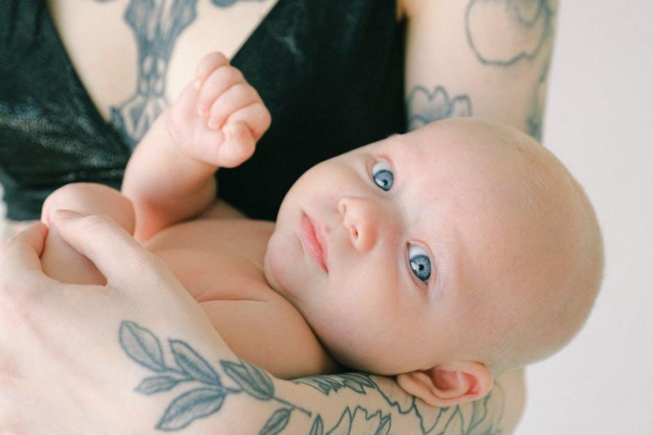 Unicona_tra_musica_e_arte_visiva_n9OazaYfbs - Confidenze24 Source: <a fref='https://www.pexels.com/@shvetsa' target='_new'>Anna Shvets</a> pexels - A beautiful baby with blue eyes held gently by tattooed arms, showcasing love and innocence.