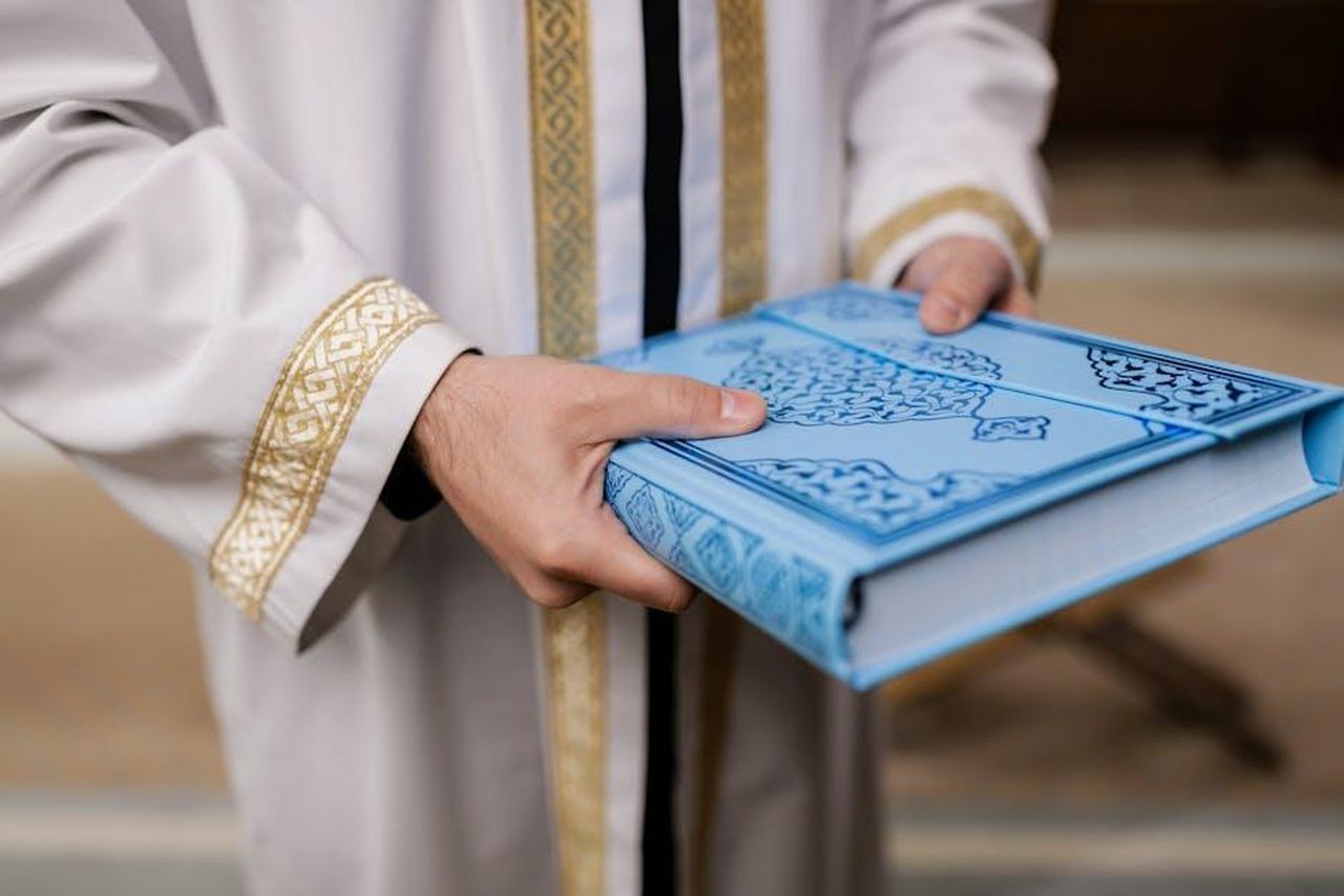 Vanessa_Scalera_ha_risposto_per_le_rime_allautrice_1zMG7ycFgN - Confidenze24 Source: Alena Darmel - pexels - Close-up of a man holding a blue Quran, dressed in a traditional robe, signifying Muslim culture and religion.