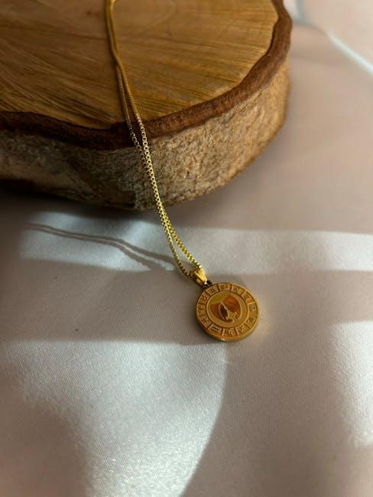 Vergine_0ACKCoviZ9 - Confidenze24 Source: Lala Jafarova - pexels - A delicate gold necklace featuring a zodiac-themed pendant, captured in natural light on wood.