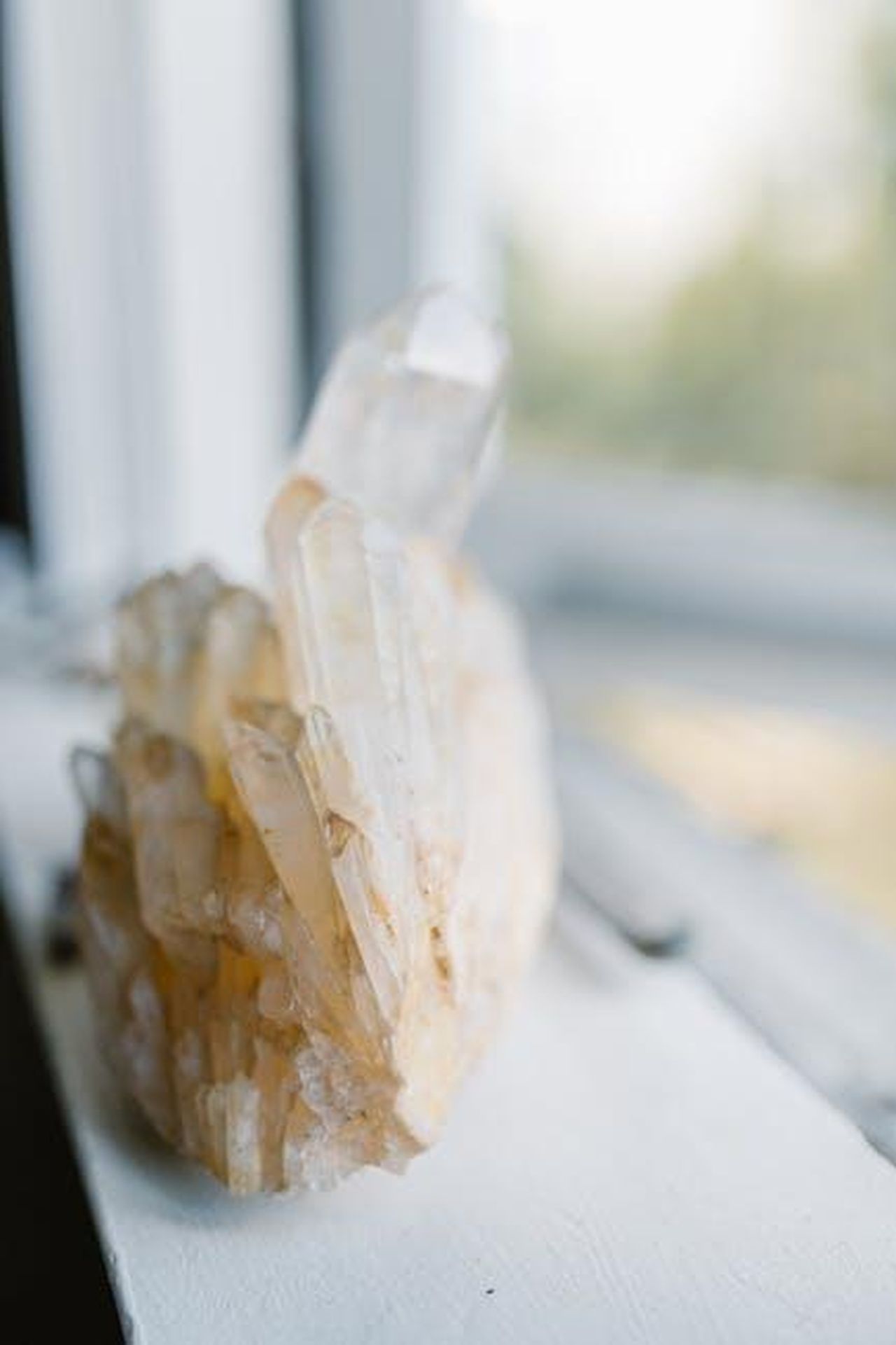 Vergine_domenica_discreta_n2rBZ1Nfh3 - Confidenze24 Source: RDNE Stock project - pexels - Close-up of a clear quartz crystal cluster on a white windowsill, radiating energy.