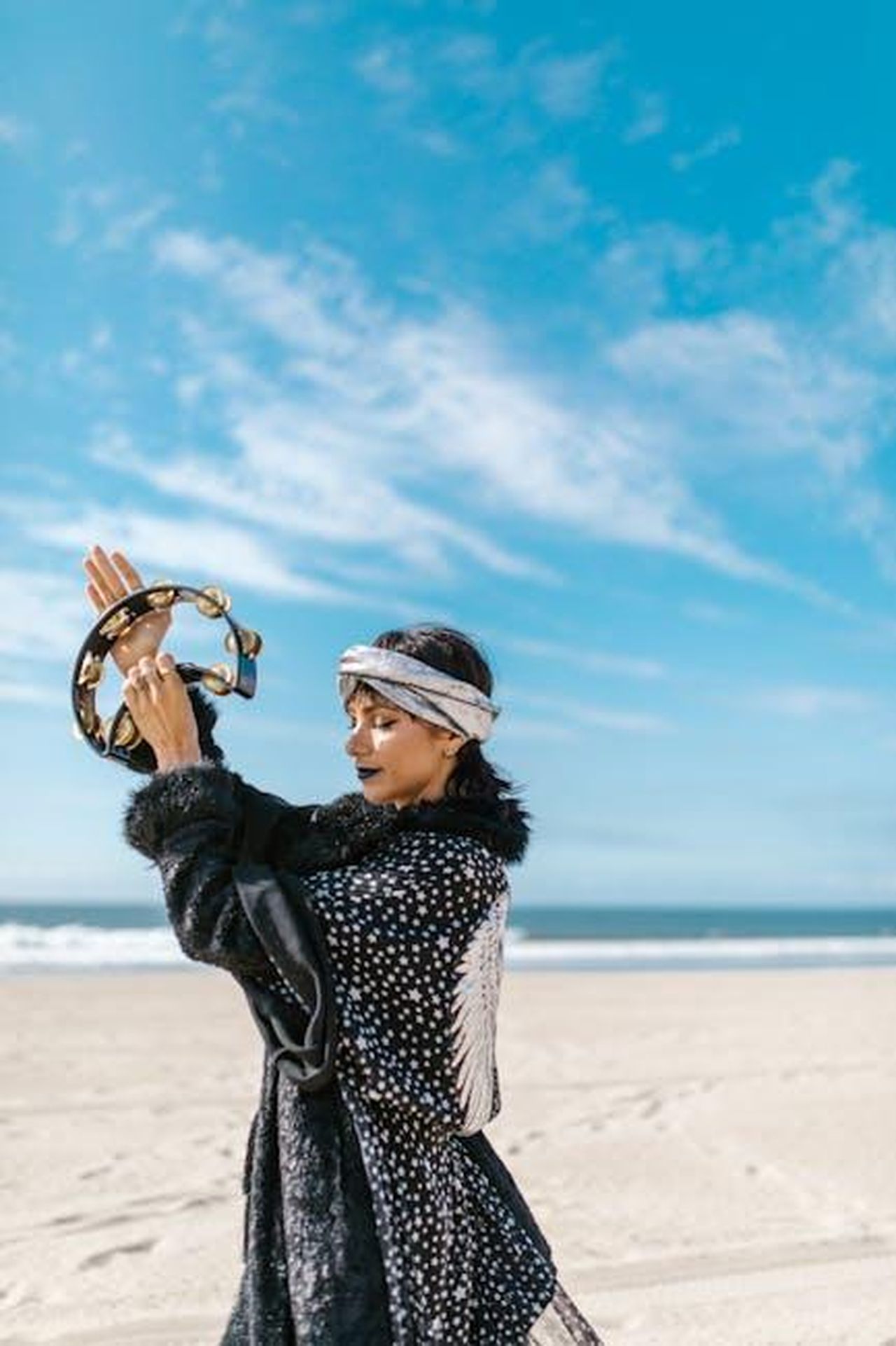 Vergine_riconsiderare_le_scelte_js8uFAfdPw - Confidenze24 Source: RDNE Stock project - pexels - A woman in bohemian attire plays a tambourine at a sunny beach.
