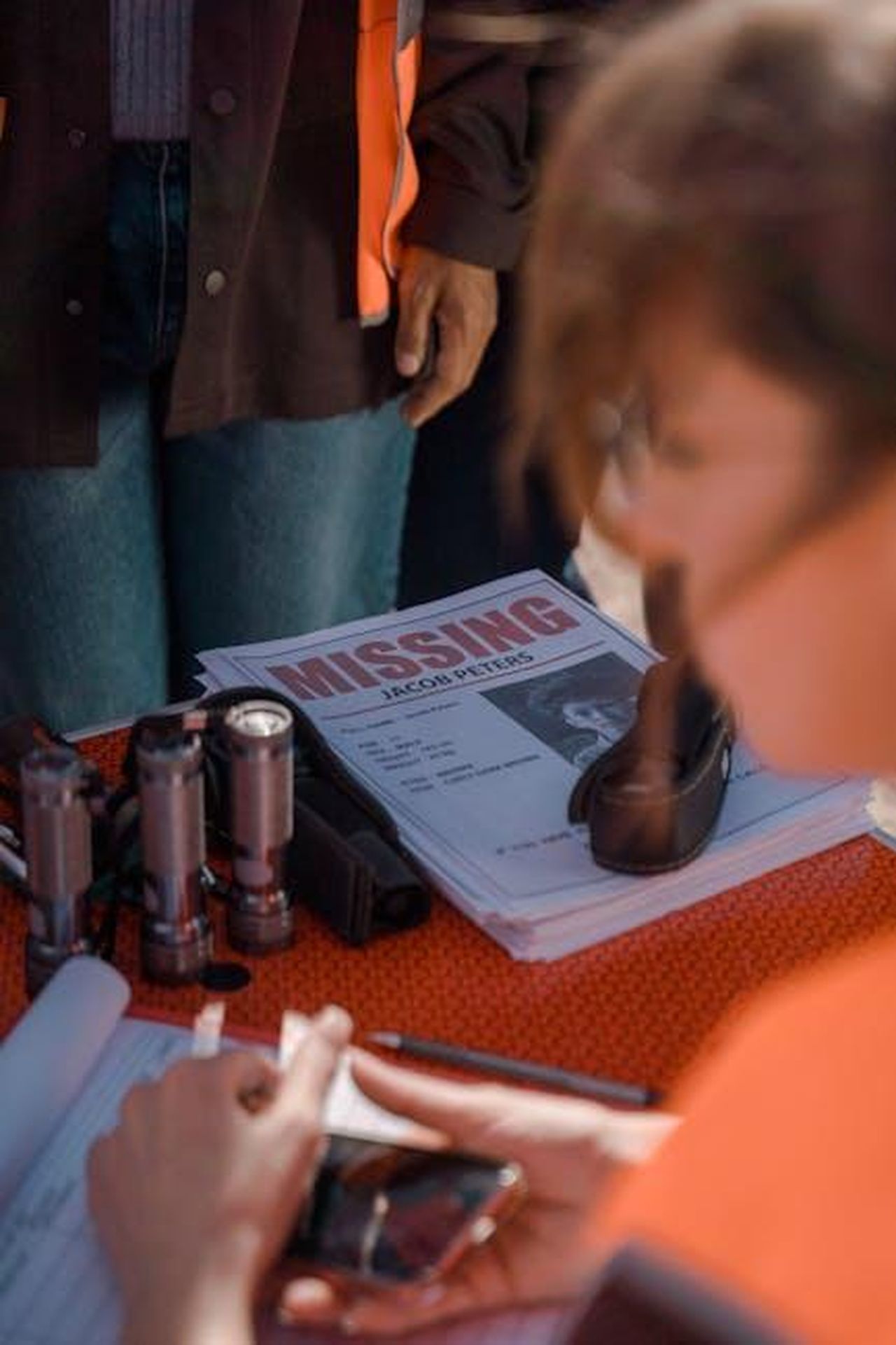 Virtudes_apprende_che_Adolfo__scomparso_coi_nonni_ZAtkzPrK5o - Confidenze24 Source: Ron Lach - pexels - Close-up of a community search gathering with missing person poster and communication devices.