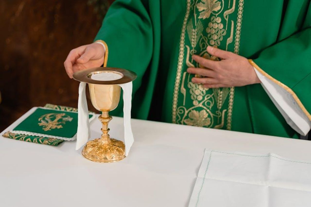 Virtudes_ruba_un_calice_doro_per_recuperare_del_denaro_XoJRPRHh7D - Confidenze24 Source: MART PRODUCTION - pexels - Close-up of a priest's hand arranging communion elements during a religious ceremony indoors.