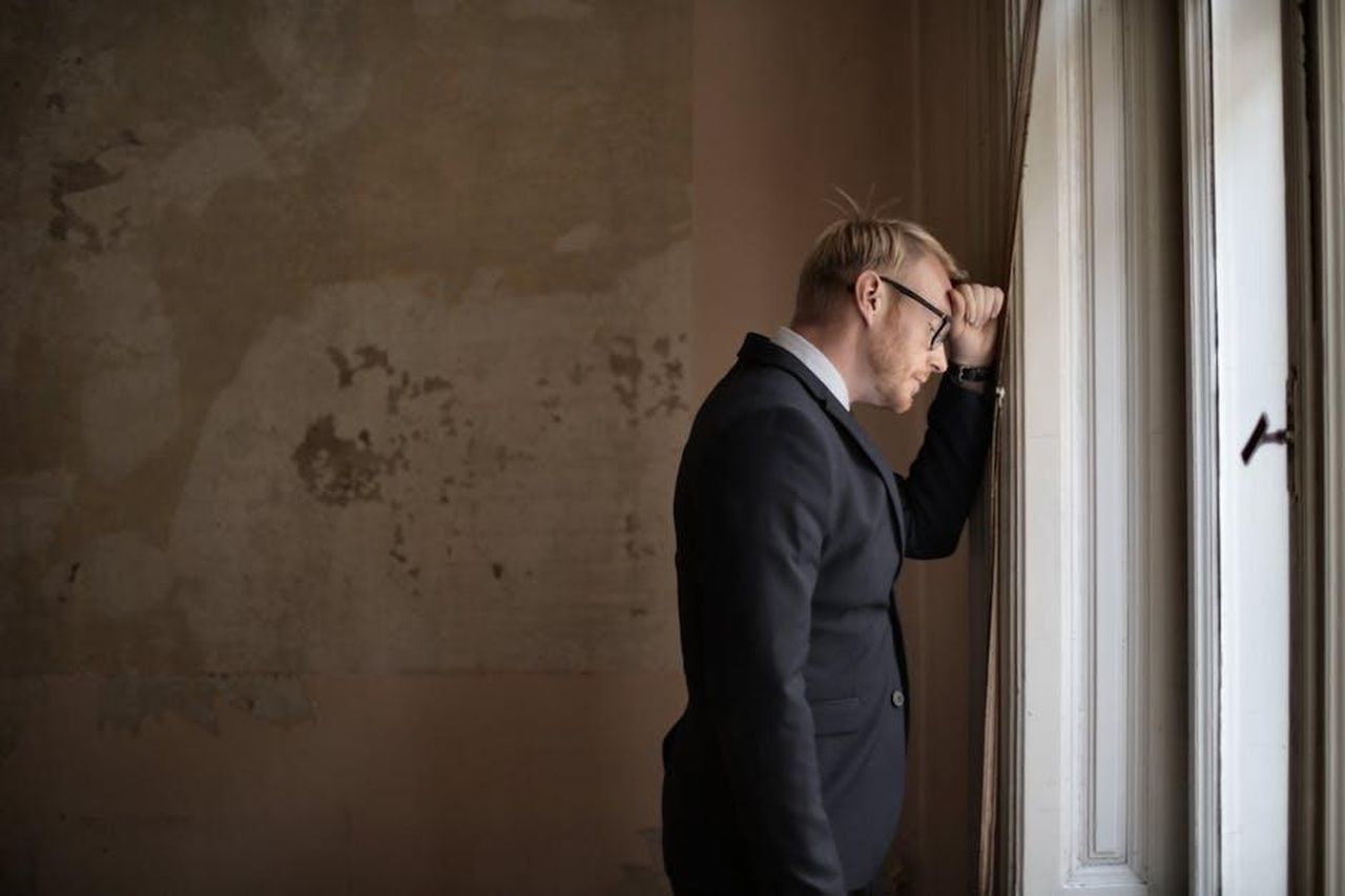 Zeudi_Di_Palma_infastidita_dagli_atteggiamenti_di_Helena_e_Javier_8JIhFofnRD - Confidenze24 Source: Andrea Piacquadio - pexels - A worried businessman in a suit leaning against a window, expressing stress and concern.