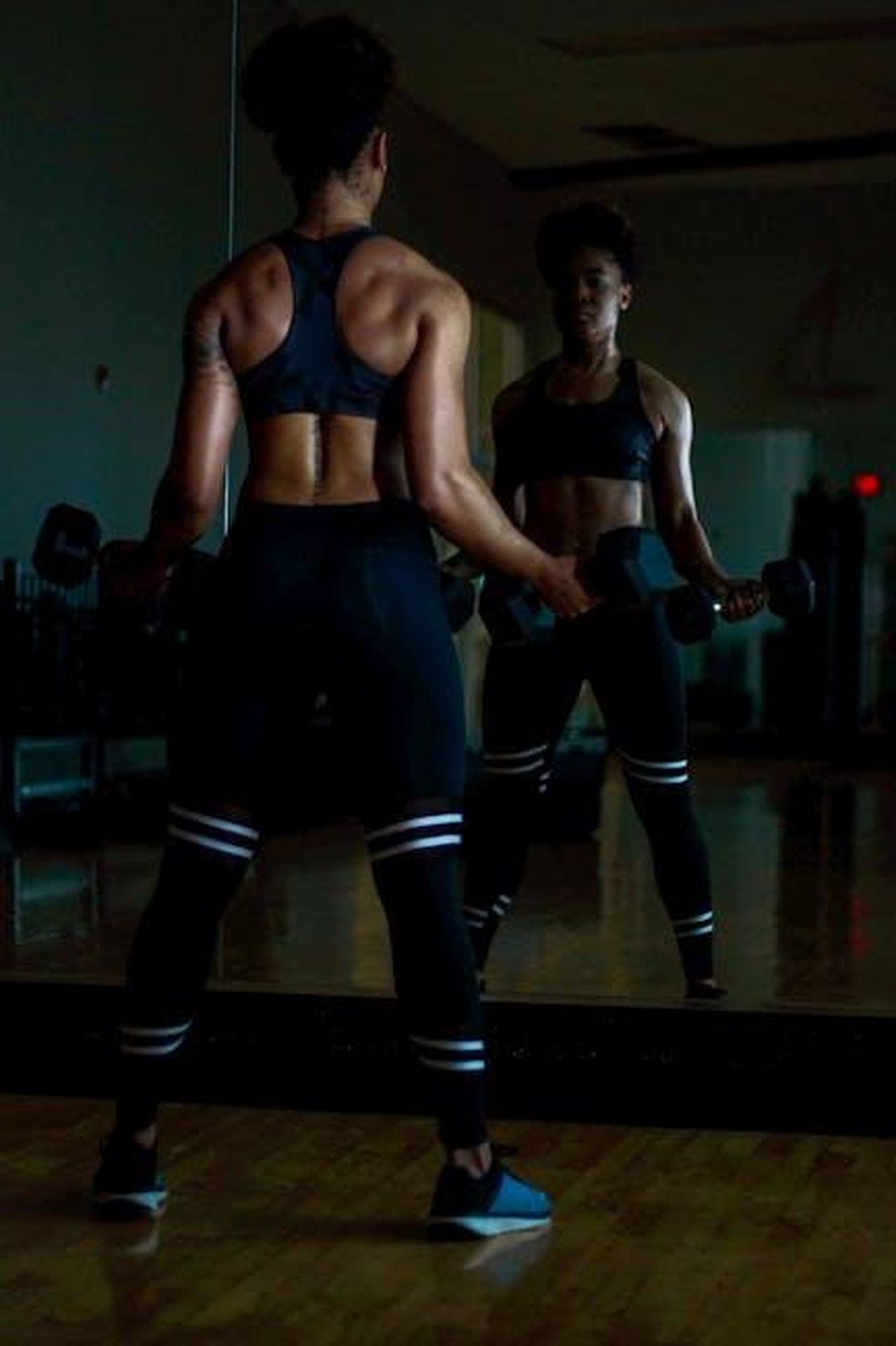 3__una_donna_forte_T3cSZjc4Pb - Confidenze24 Source: Eduardo Romero - pexels - A determined woman lifting weights in a gym while looking at her reflection in a mirror.