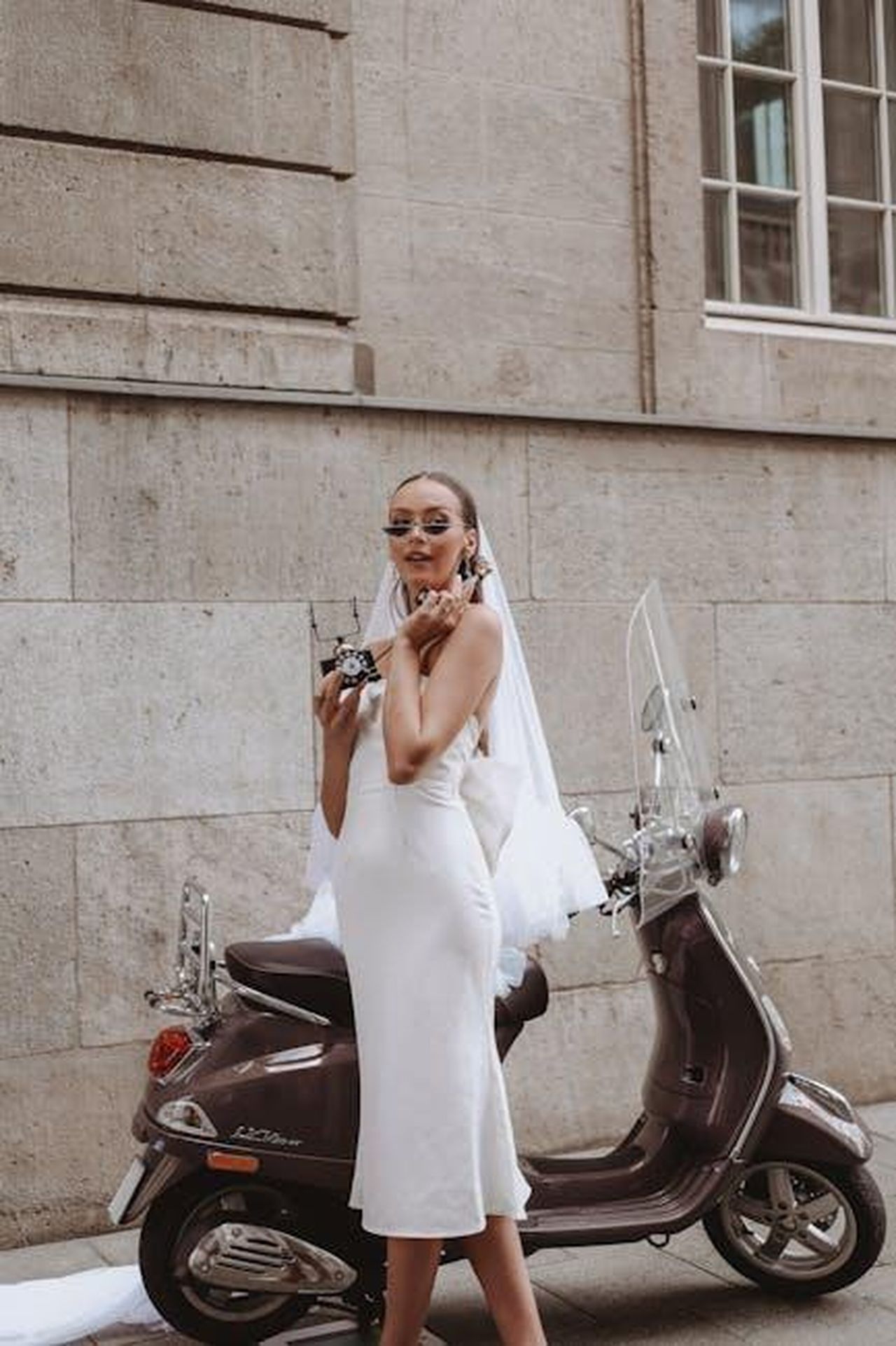 Abito_midi_in_jersey_Tencel_con_nodo_laterale_e6H9AcjDLP - Confidenze24 Source: Erva Nur - pexels - Stylish bride in wedding dress poses with vintage phone and scooter in urban Cologne.