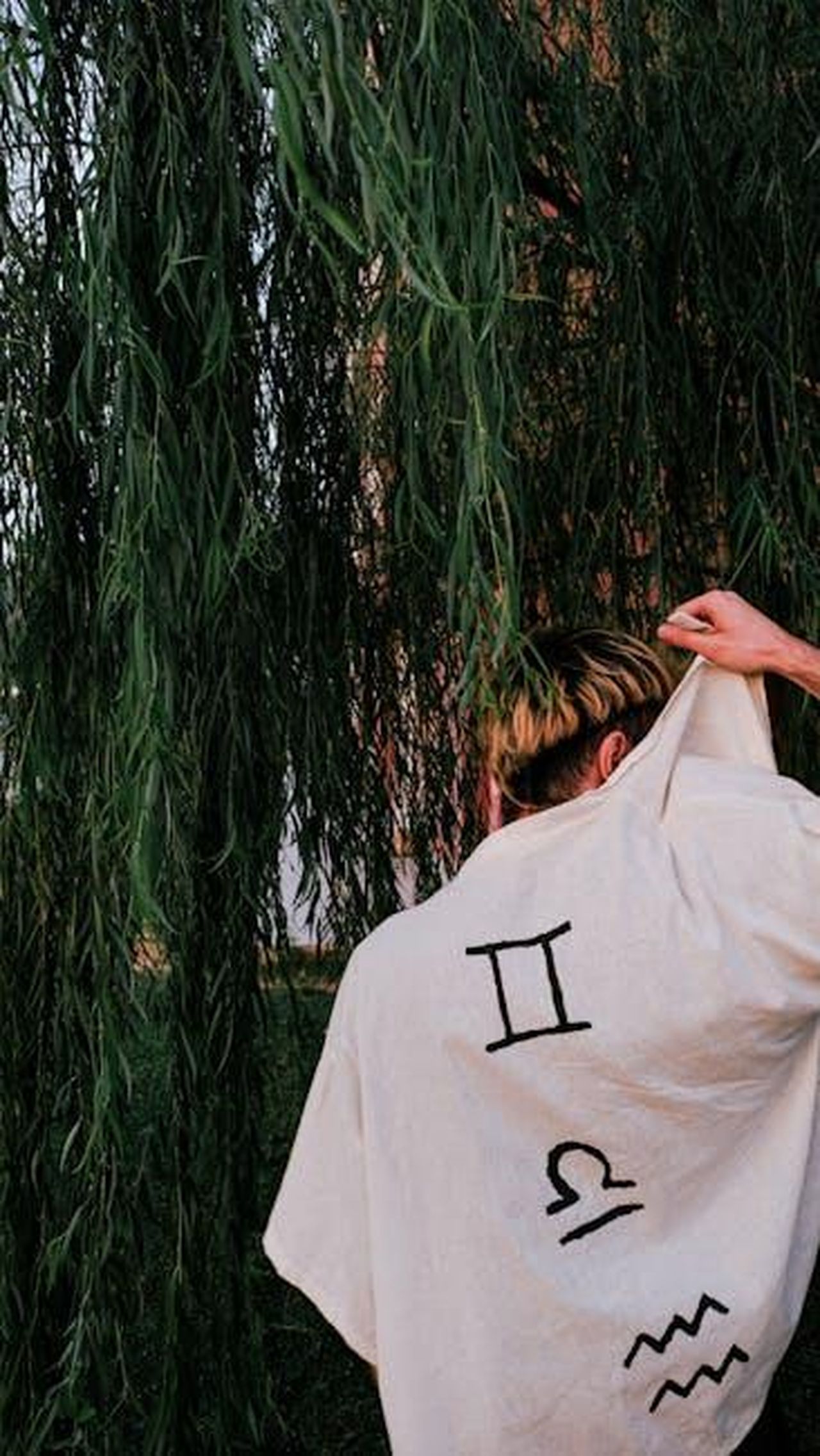 Acquario_20_gennaio__18_febbraio_nGnNxeFFAt - Confidenze24 Source: armağan başaran - pexels - Person with zodiac symbols on shirt standing under willow tree outdoors.