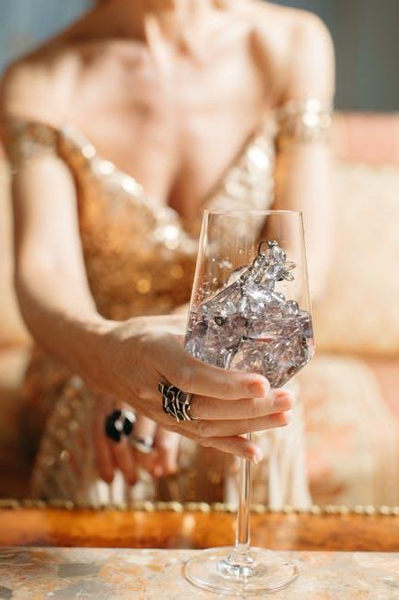 Aggiornamenti_su_Tiger_Woods_e_altri_eventi_celebri_Ck8q9DaYf3 - Confidenze24 Source: Anastasia Shuraeva - pexels - A woman in a gold dress holds a wine glass filled with crystals, exuding luxury and sophistication.