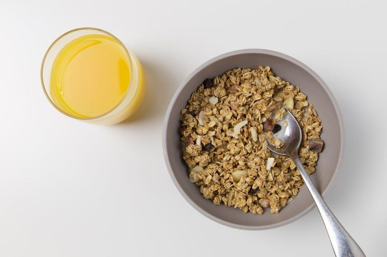 Aggiungi_Fibra_alla_Tua_Dieta_per_Gestire_il_Peso_E9GK4NK8mY - Confidenze24 Source: Foodie Factor - pexels - A top view of granola in a bowl with a spoon and a glass of orange juice on a white background.
